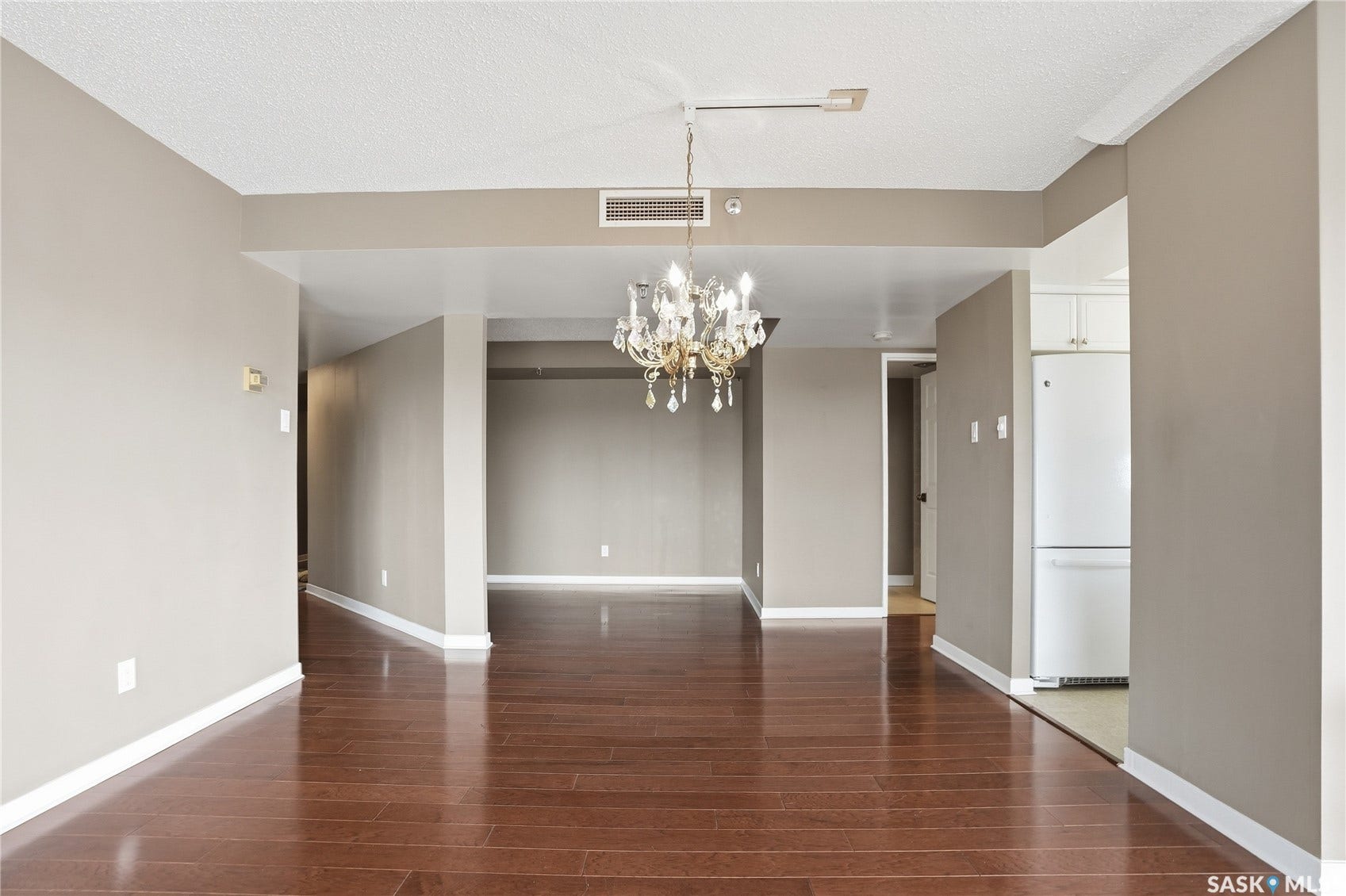 Rich wood-finish flooring throughout, neutral wall tones, and an ornate chandelier