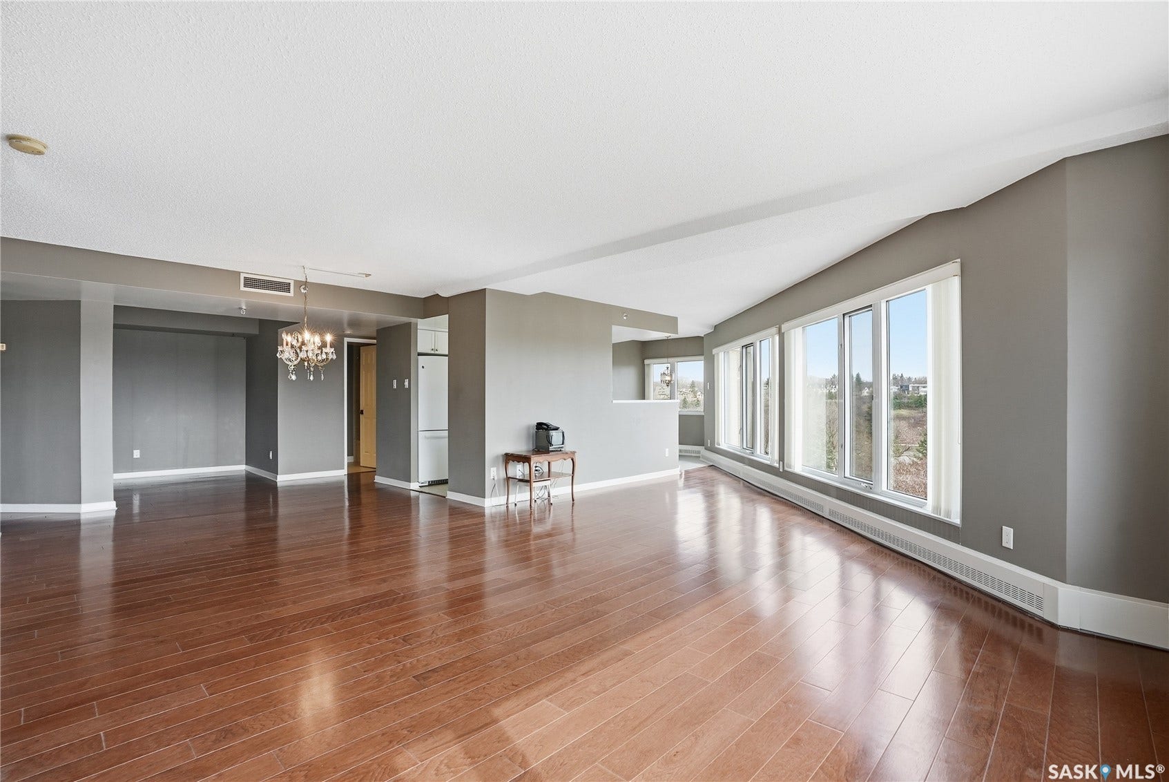 Expansive living Hardwood flooring throughout, recessed ceiling with a chandelier, and an integrated air conditioning ventarea featuring wood-finish flooring, a full wall of windows, and a chandelier light fixture
