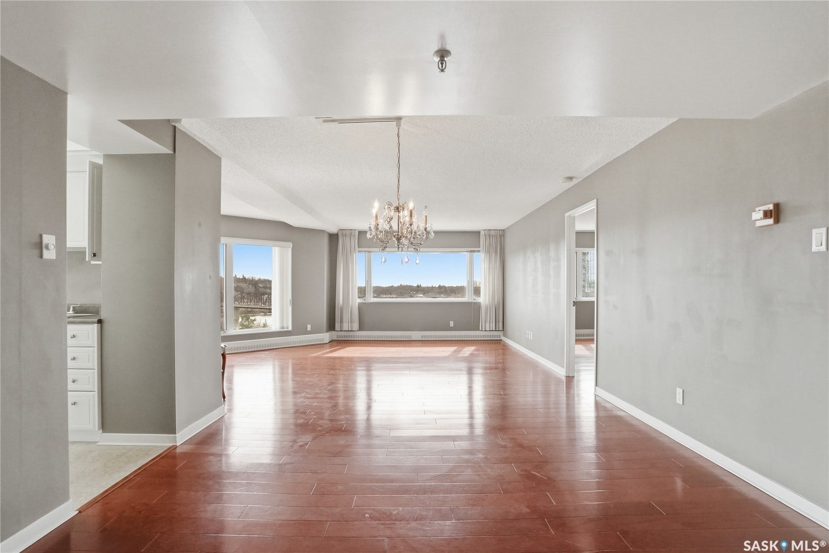 Expansive room featuring wood-finish flooring, a tiered crystal chandelier, and multiple windows