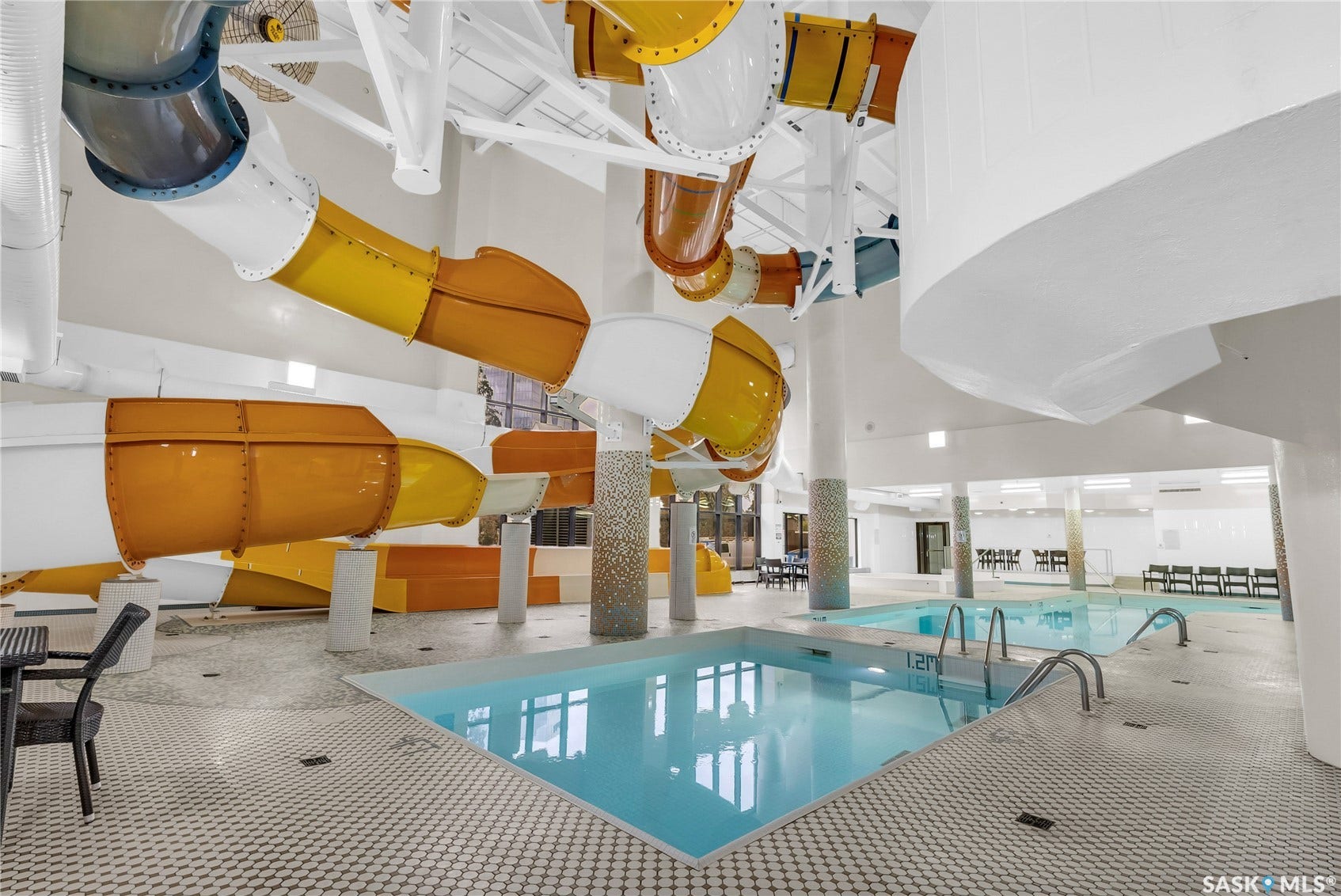 Indoor aquatic facility featuring multiple water slides, two pools with integrated steps, and mosaic-tiled support columns