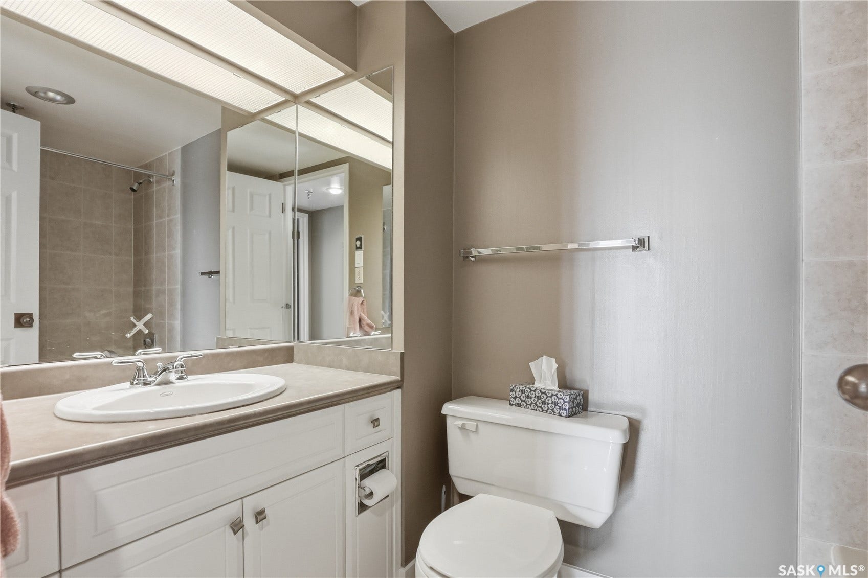 Vanity with integrated sink, chrome faucet, white cabinetry with silver hardware, large mirrored wall, and overhead lighting