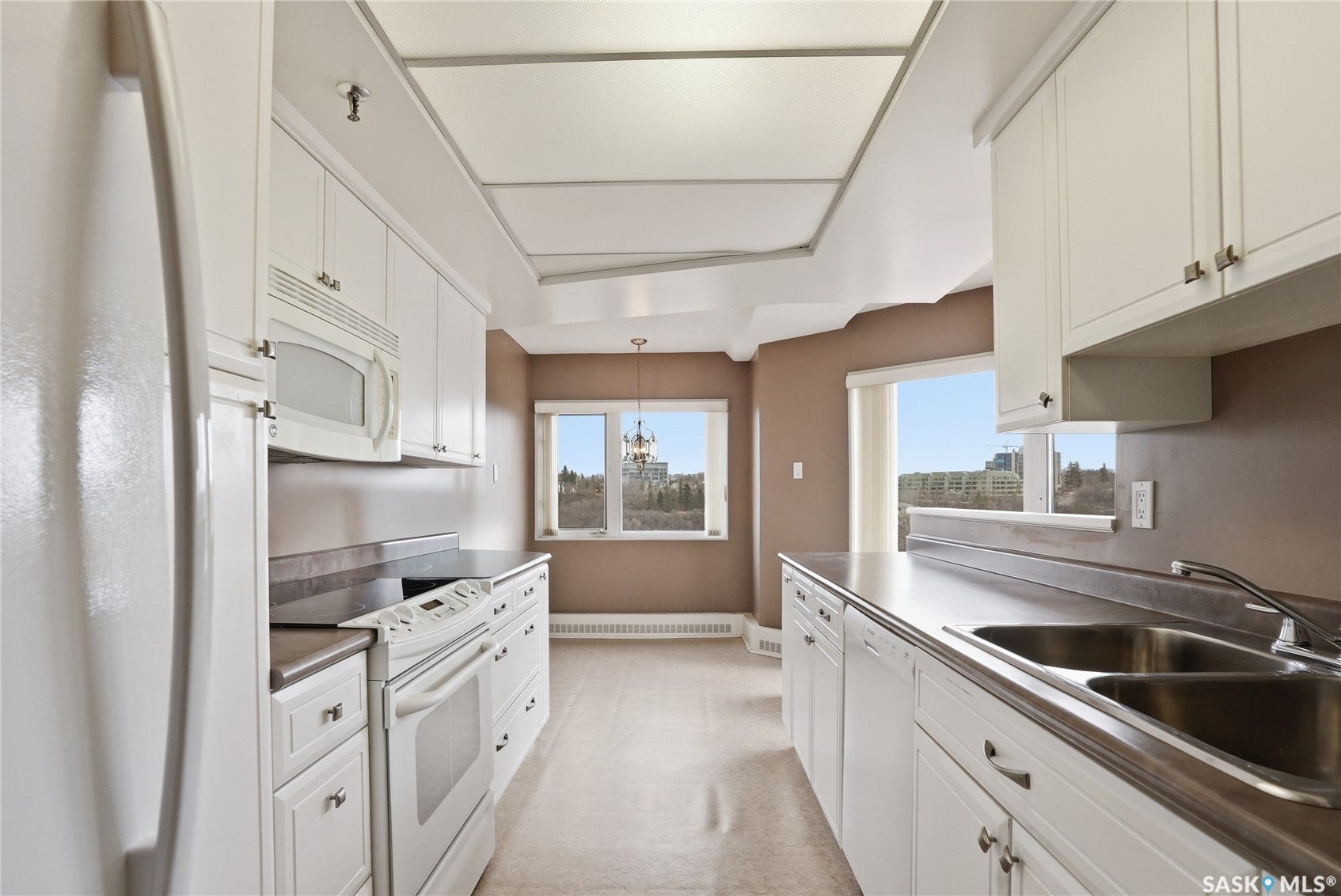 Galley kitchen featuring white cabinetry, integrated appliances, and a dual basin stainless steel sink