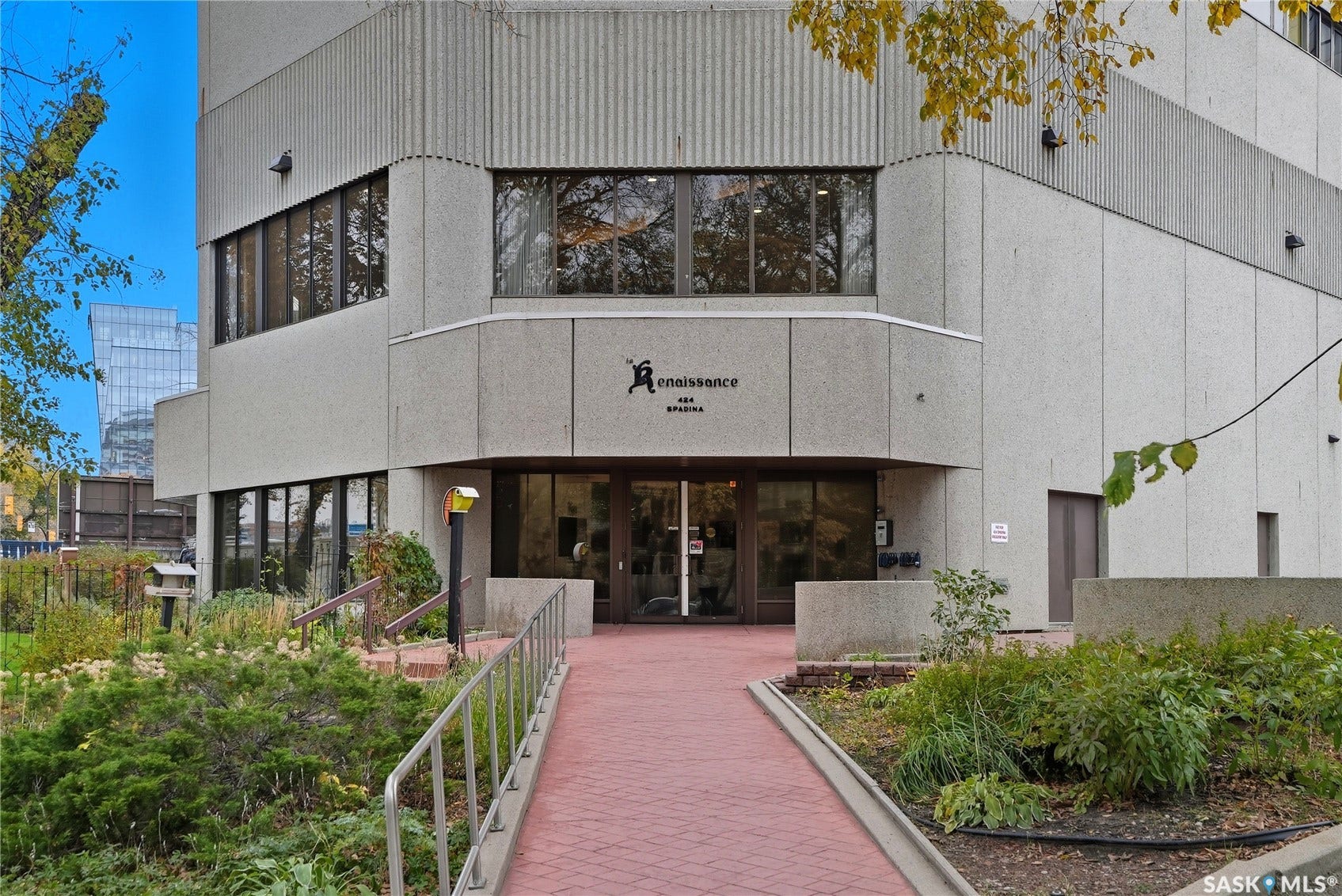 Concrete facade building featuring multiple levels of windows, a central entrance with double doors, a red brick pathway, and metal handrails