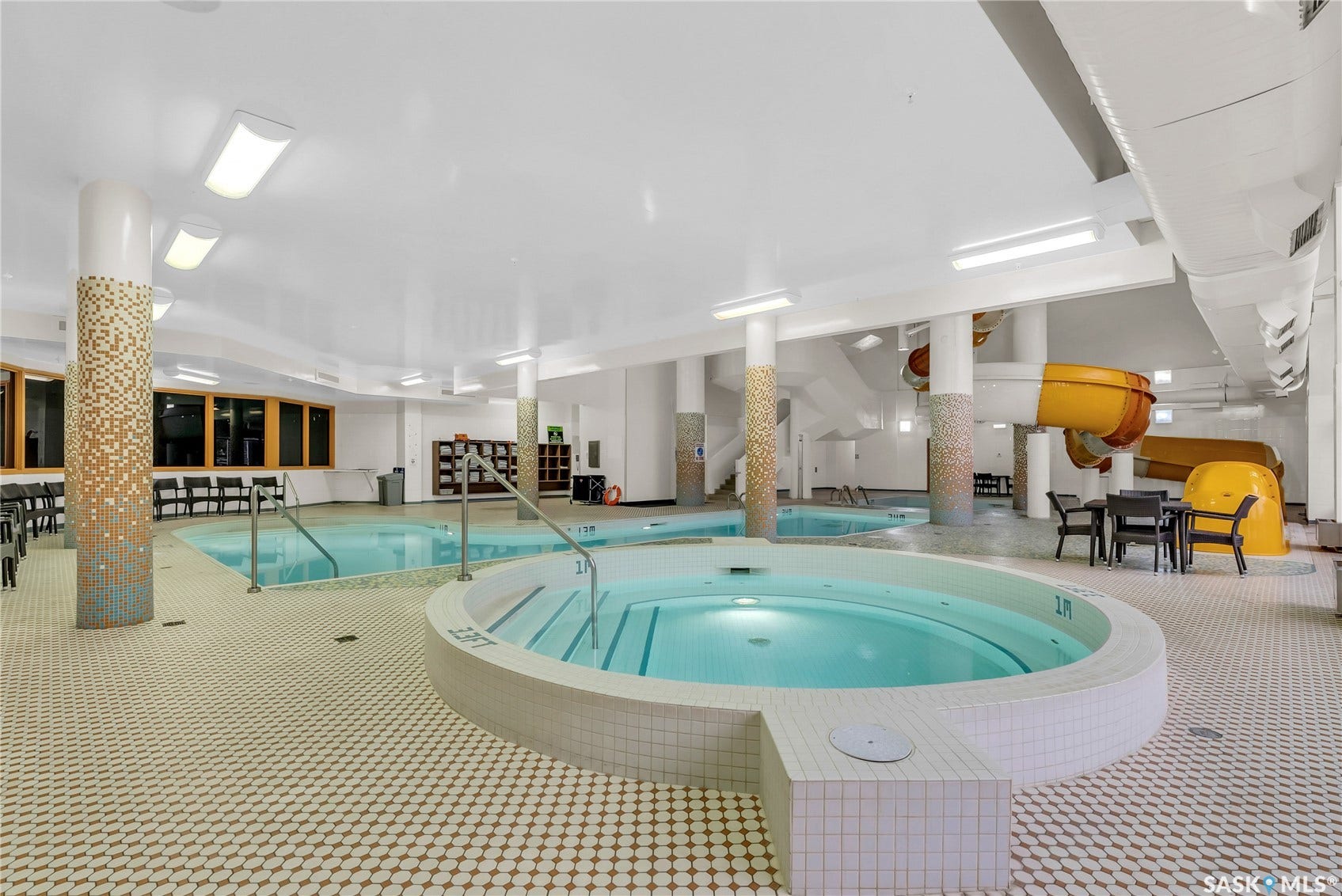 Indoor aquatic area featuring a circular spa, multiple pools, an enclosed waterslide, and mosaic-tiled columns