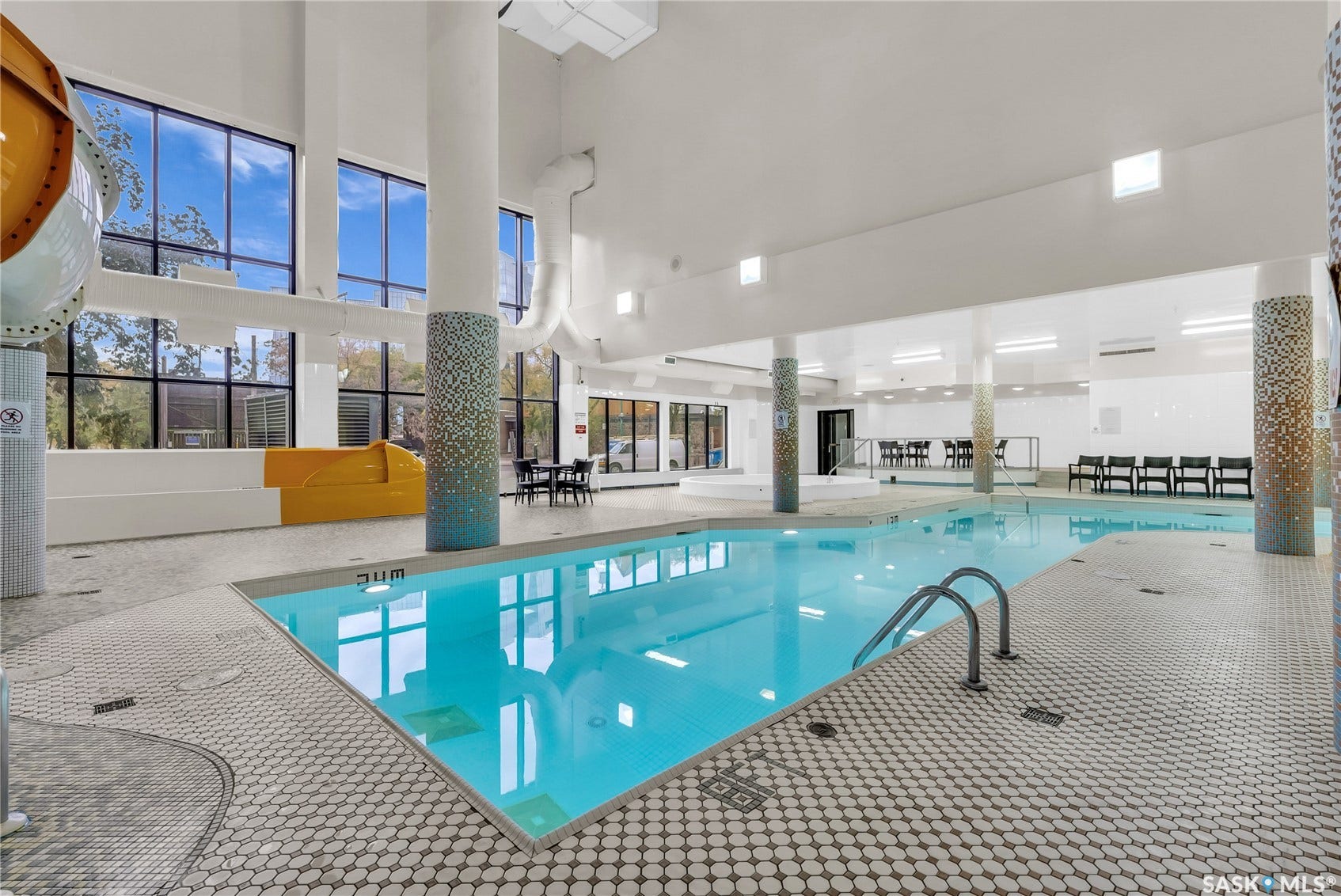 Indoor pool featuring a water slide, white tiled flooring, and high ceilings with expansive windows
