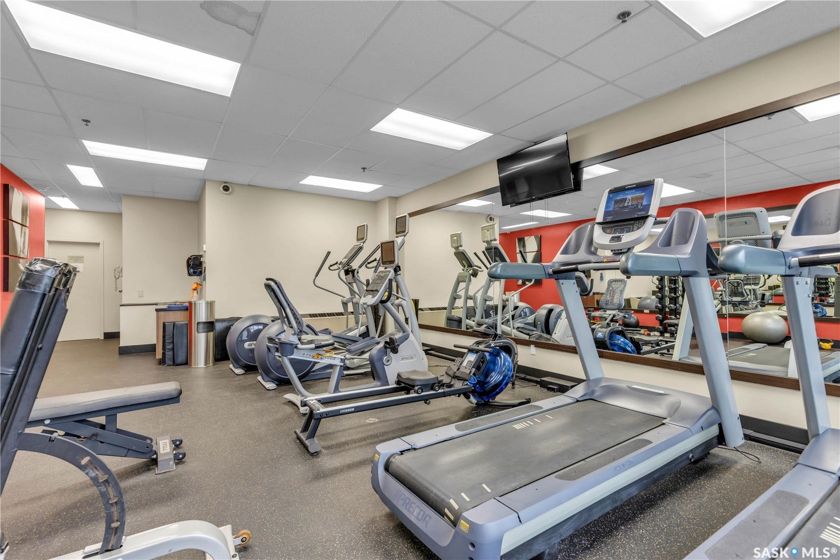Fitness facility featuring cardio equipment, rubber-surface flooring, full-wall mirrors, and recessed ceiling lighting