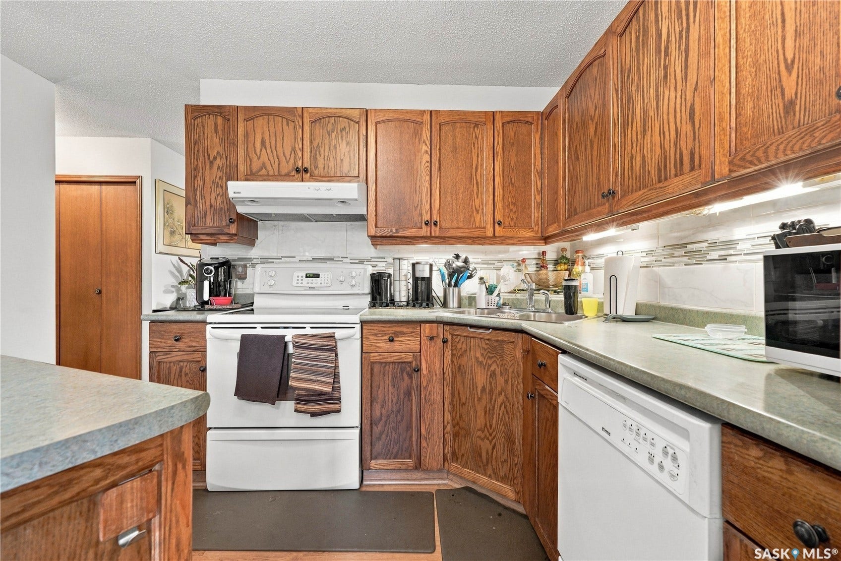 Kitchen featuring wood-finish cabinetry, white appliances, and a tile backsplash