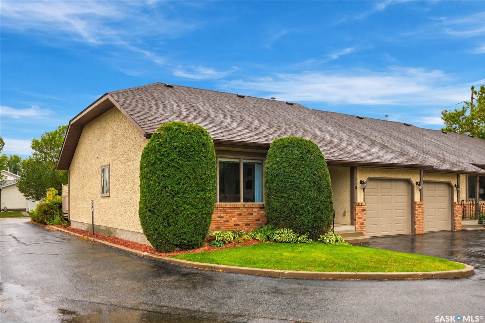 Stucco exterior with brick detailing, asphalt shingle roof, attached garages, and mature landscaping