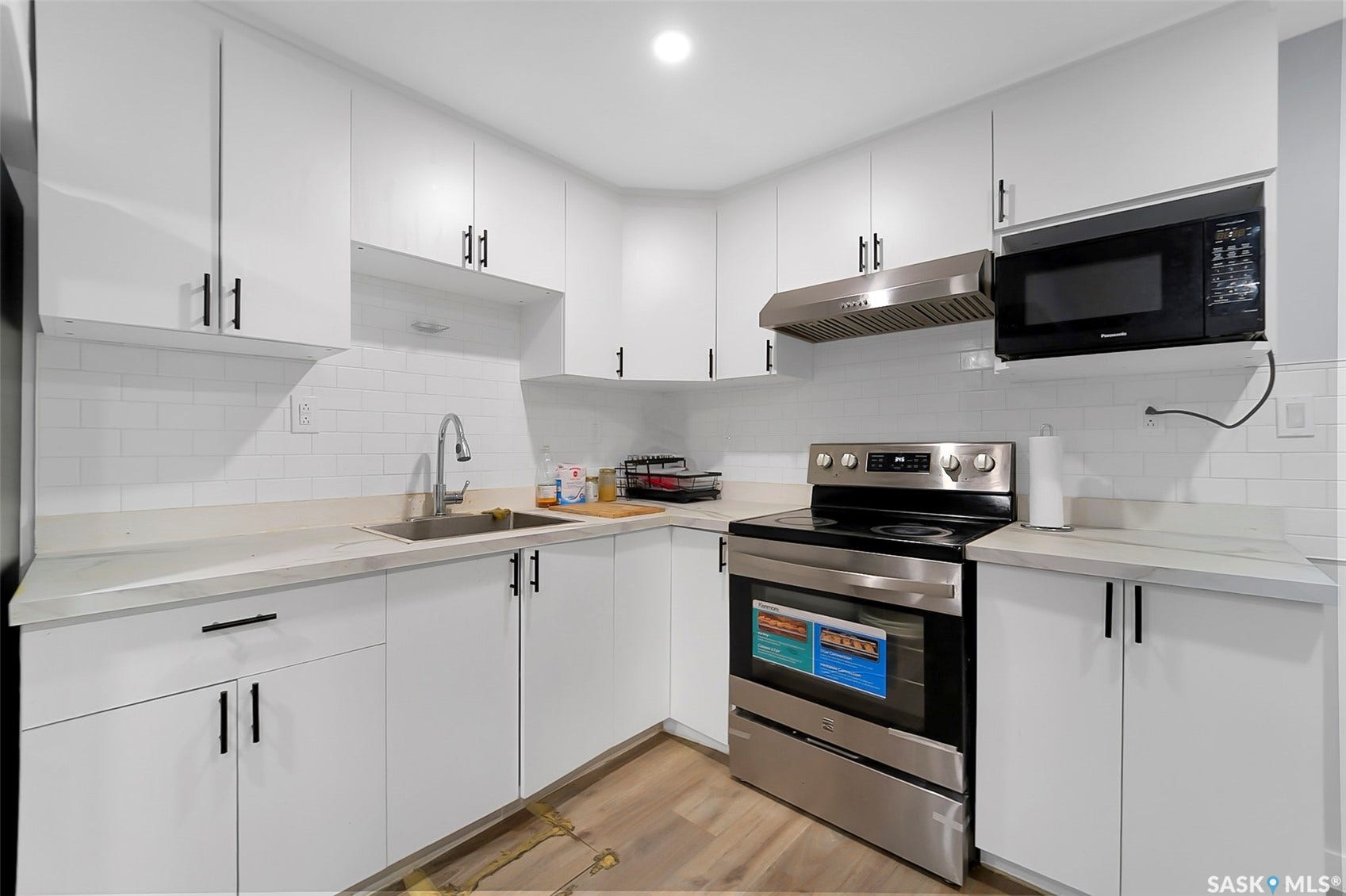 Modern kitchen featuring white cabinetry with matte black hardware, stainless steel appliances, white subway tile backsplash, and light-toned countertops