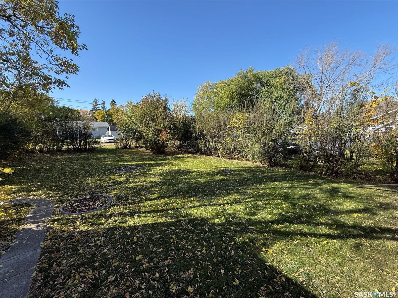 Expansive green lawn, mature trees, established shrubs, and a circular paved area