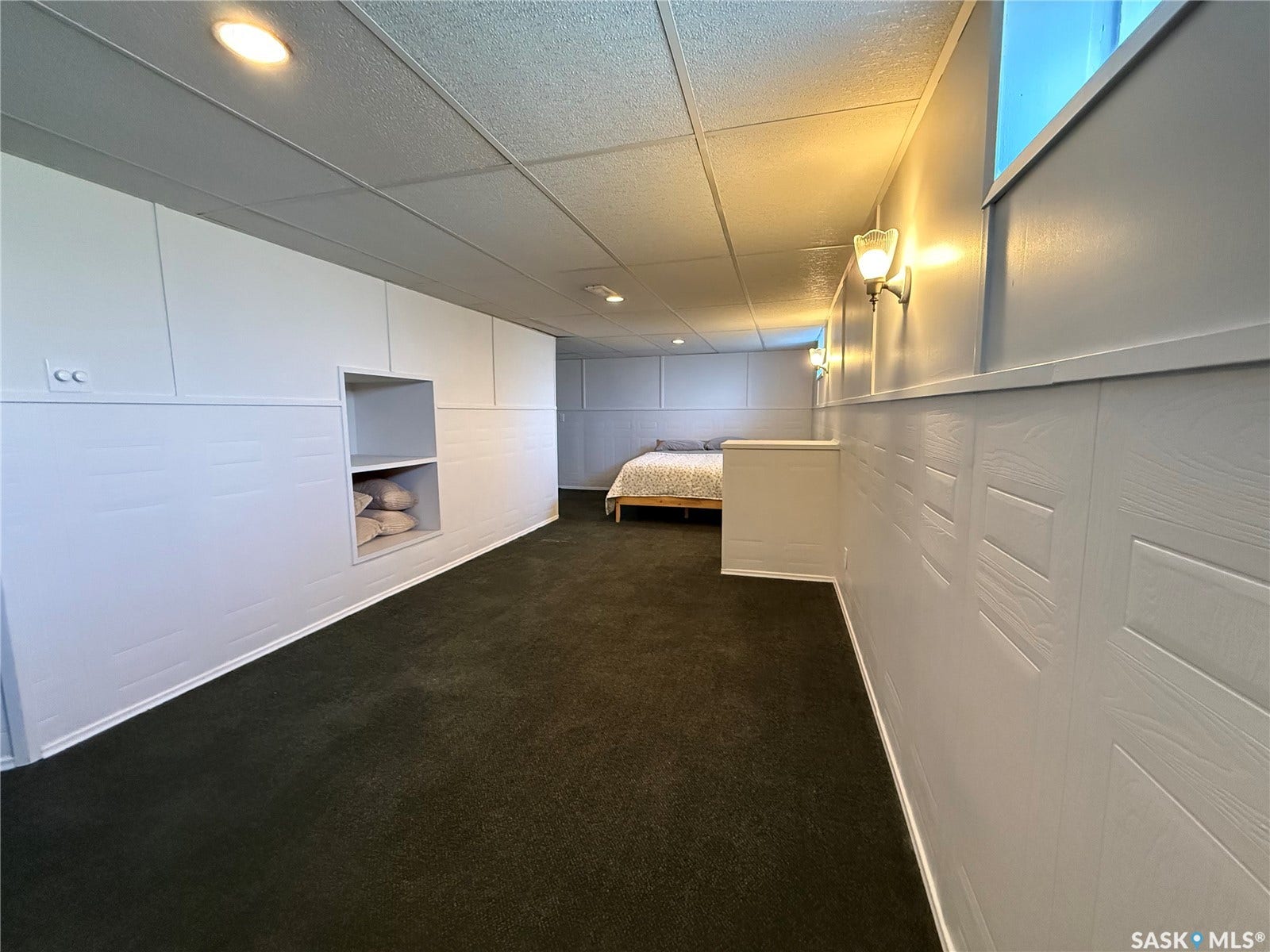White paneled walls with integrated shelving, dark carpeting, and recessed lighting