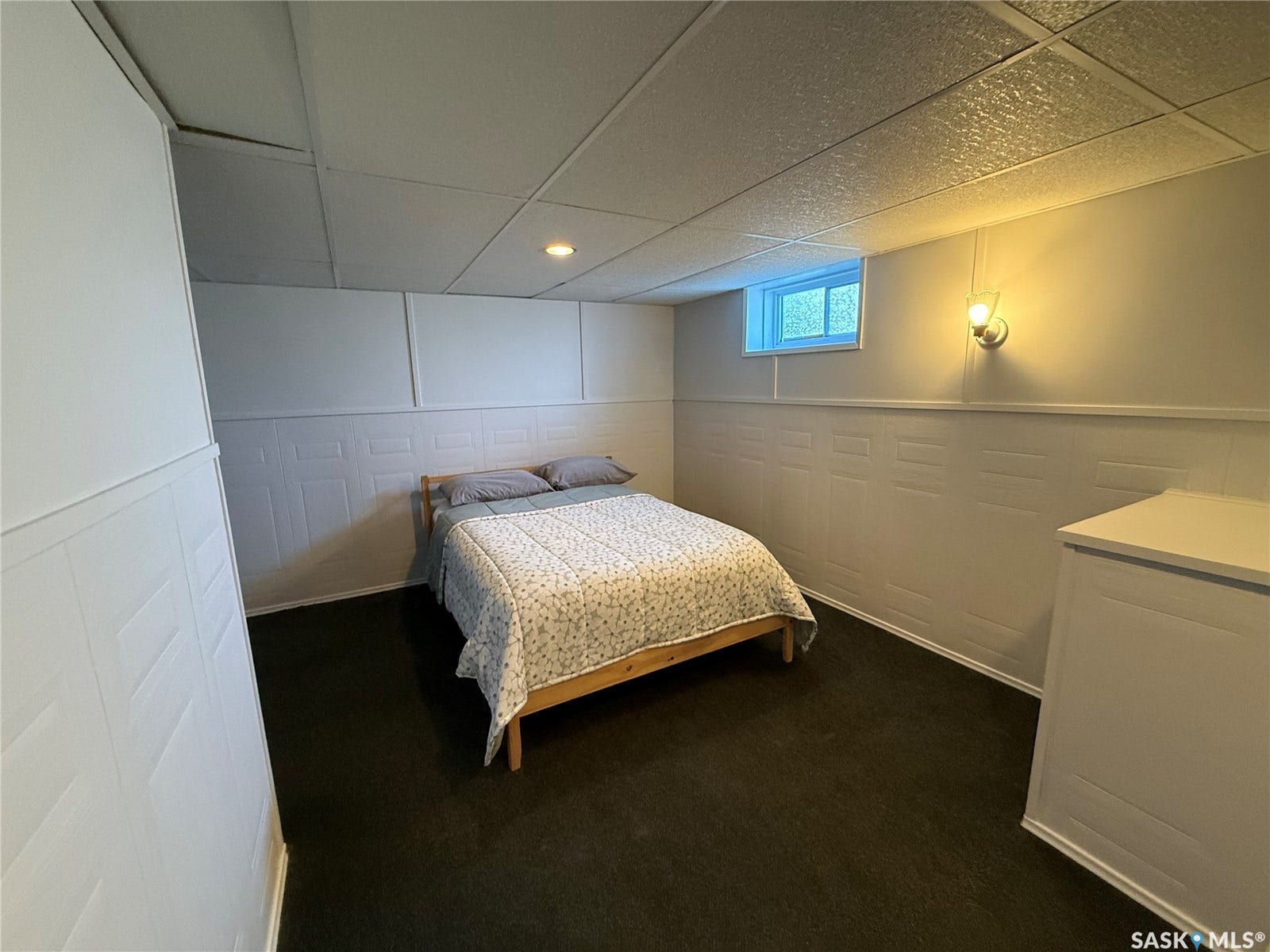 White paneling, drop ceiling with recessed lighting, wall-mounted sconce, and dark flooring