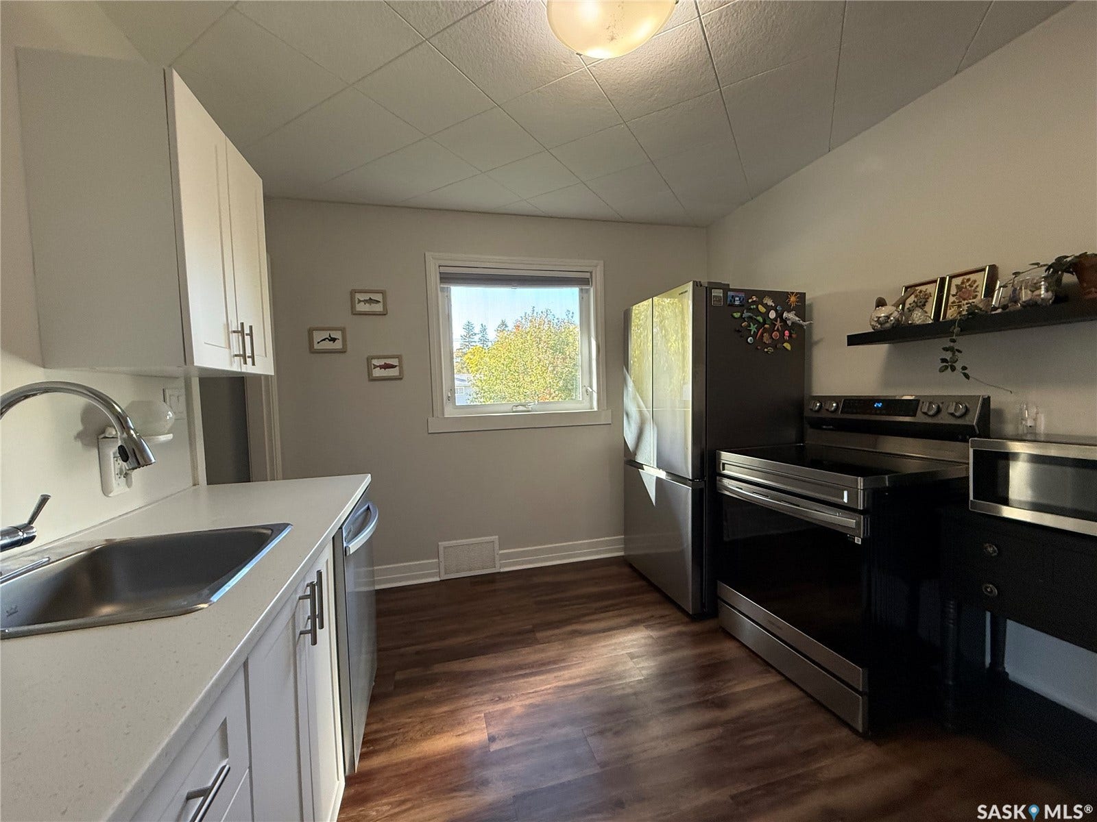 White cabinetry, stainless steel appliances, wood-finish flooring, light countertop, and a window