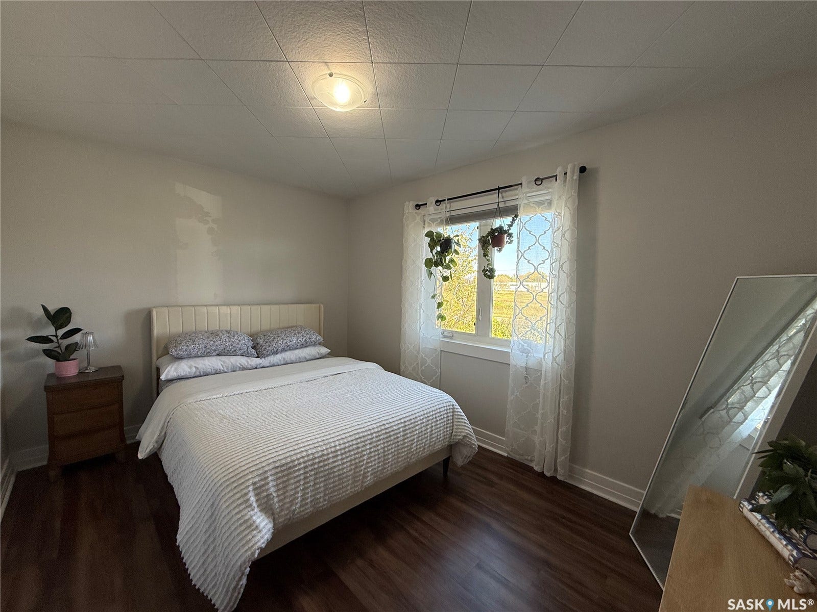 Wood-finish flooring, single window with sheer white curtains, recessed ceiling light fixture, and light-toned wall paint
