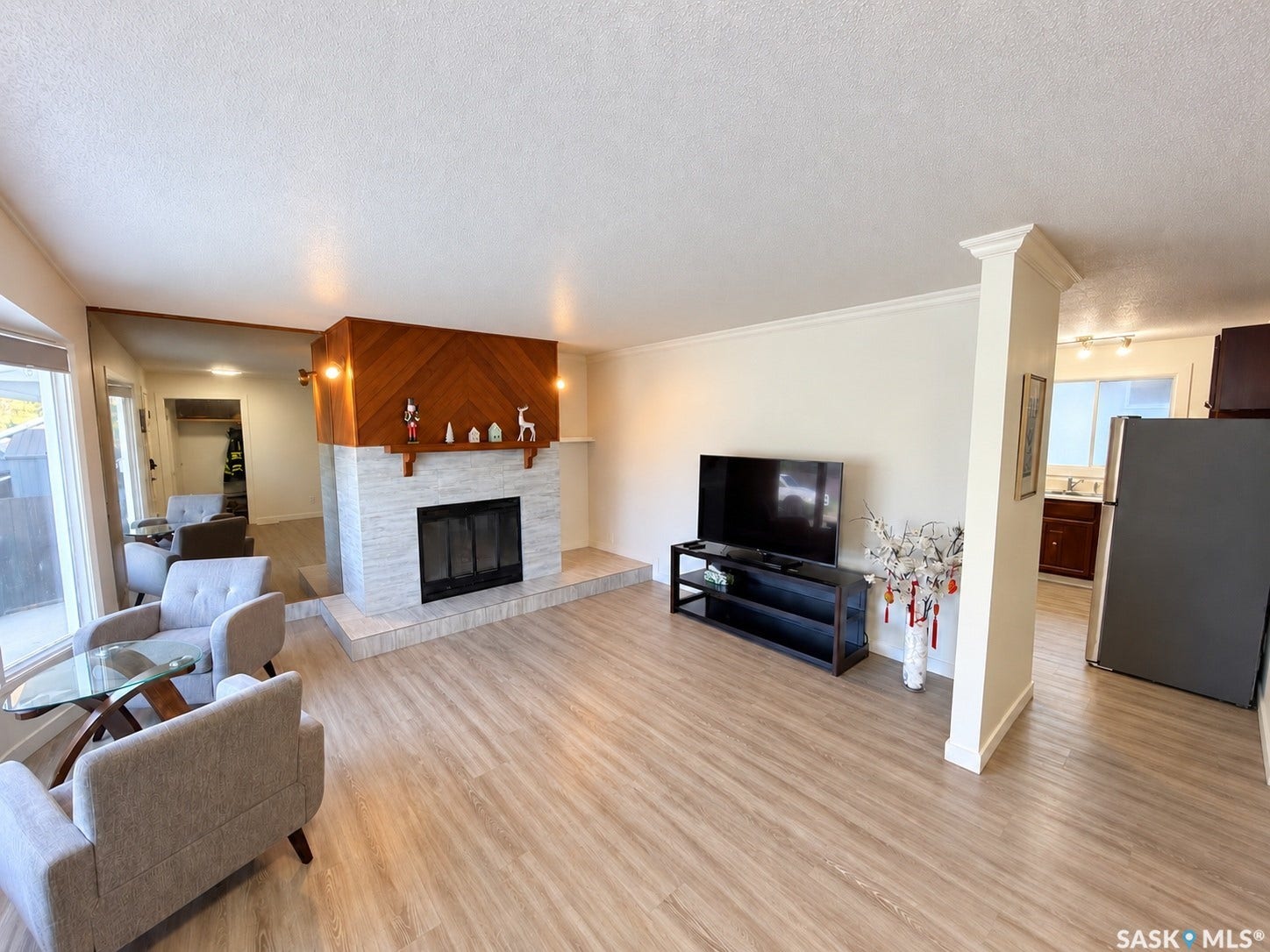Wood-finish flooring throughout, a fireplace with a stone surround, wood accent paneling, and an open layout to the kitchen