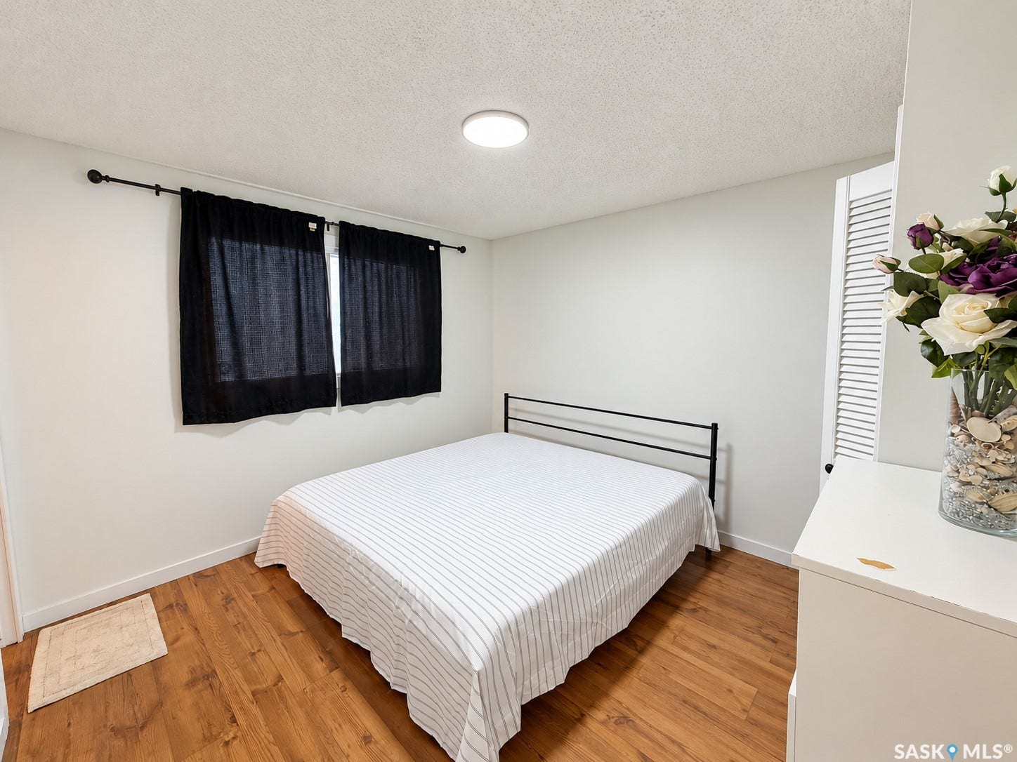 Wood-finish flooring, white walls, flush mount ceiling light, and a window with curtain rod