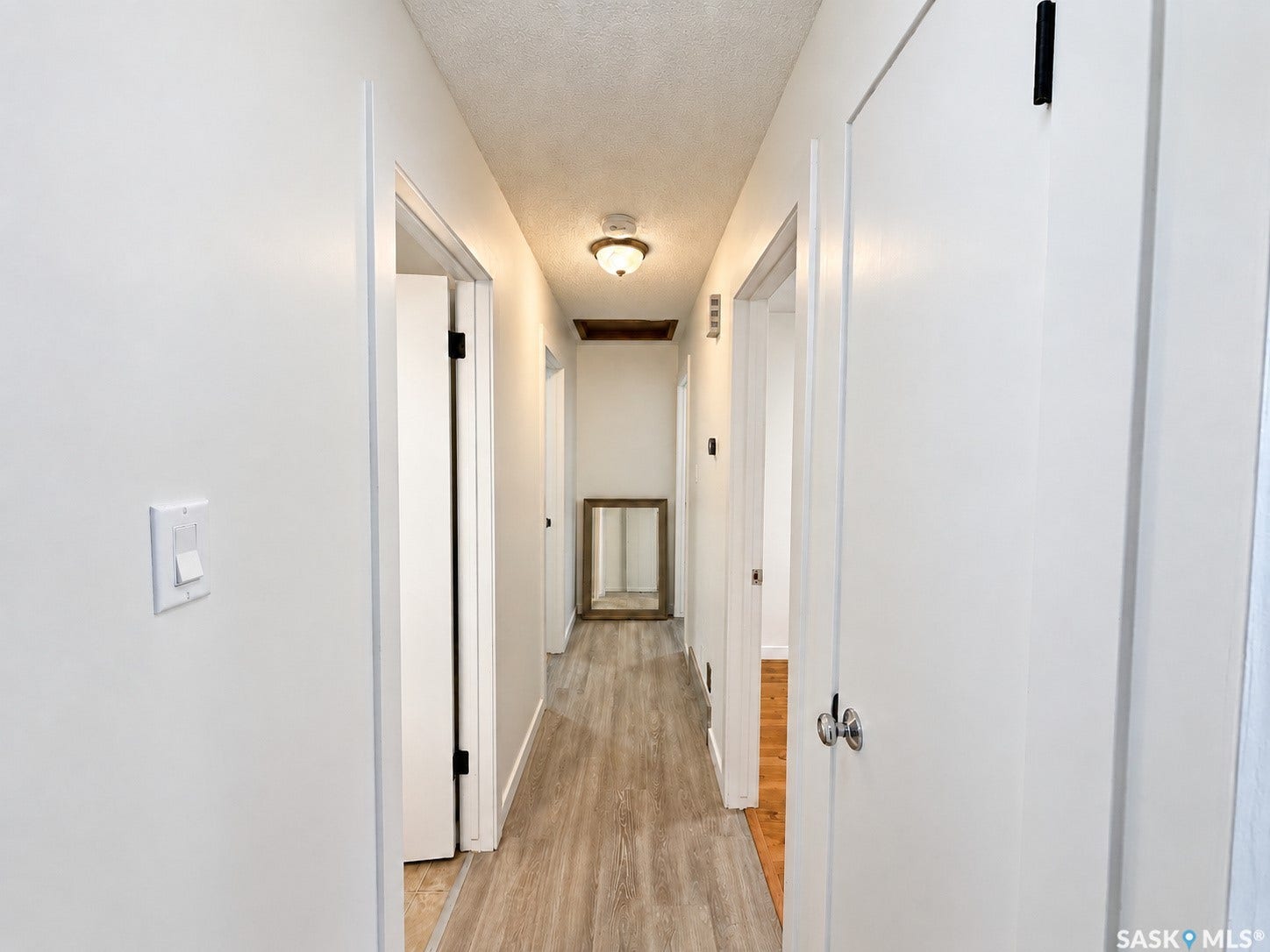 Hallway featuring wood-finish flooring, white walls, and white doors with black hardware