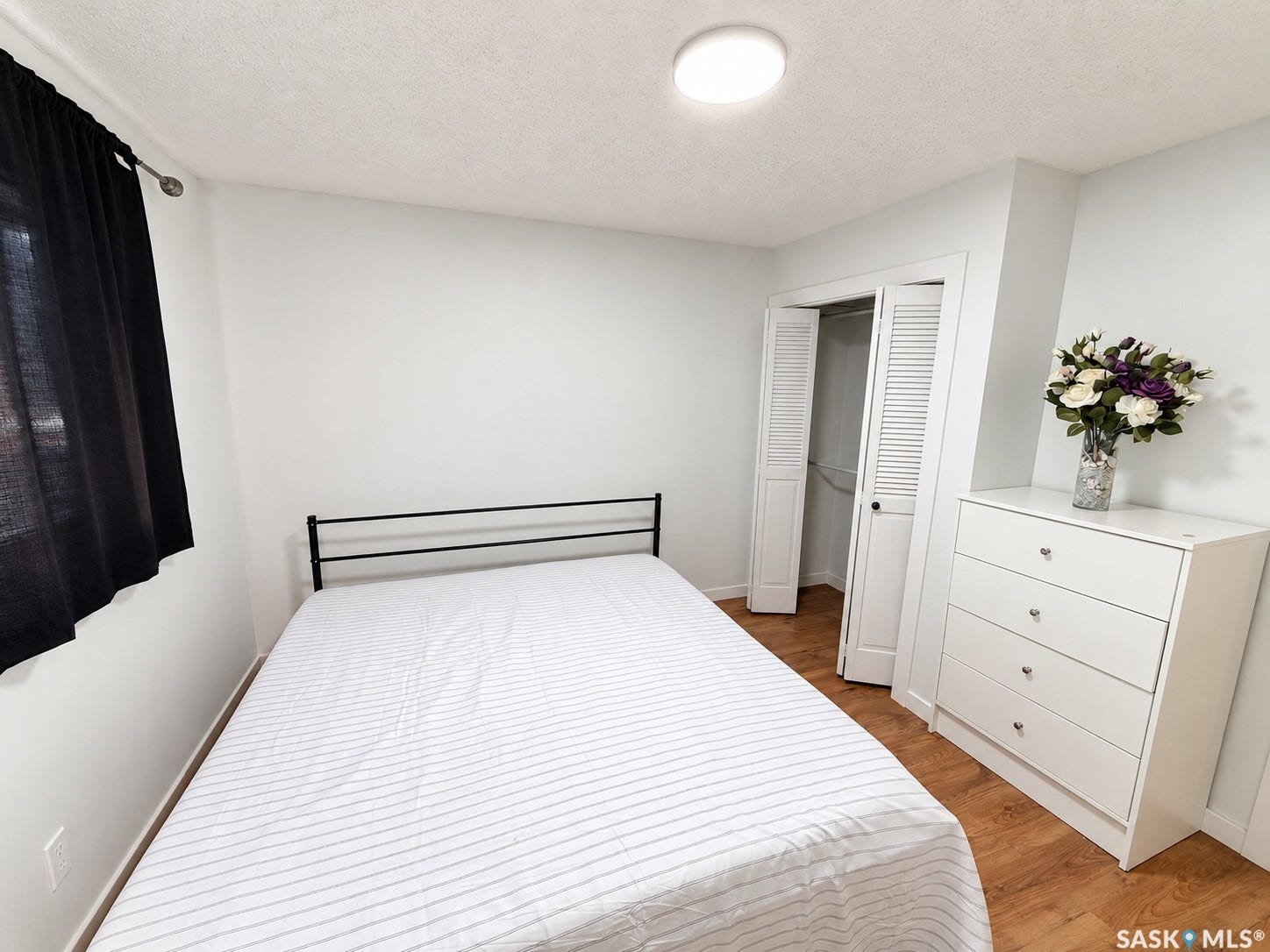 Hardwood-finish flooring, built-in closet with louvered bifold doors, recessed lighting, and a window with dark curtain rod