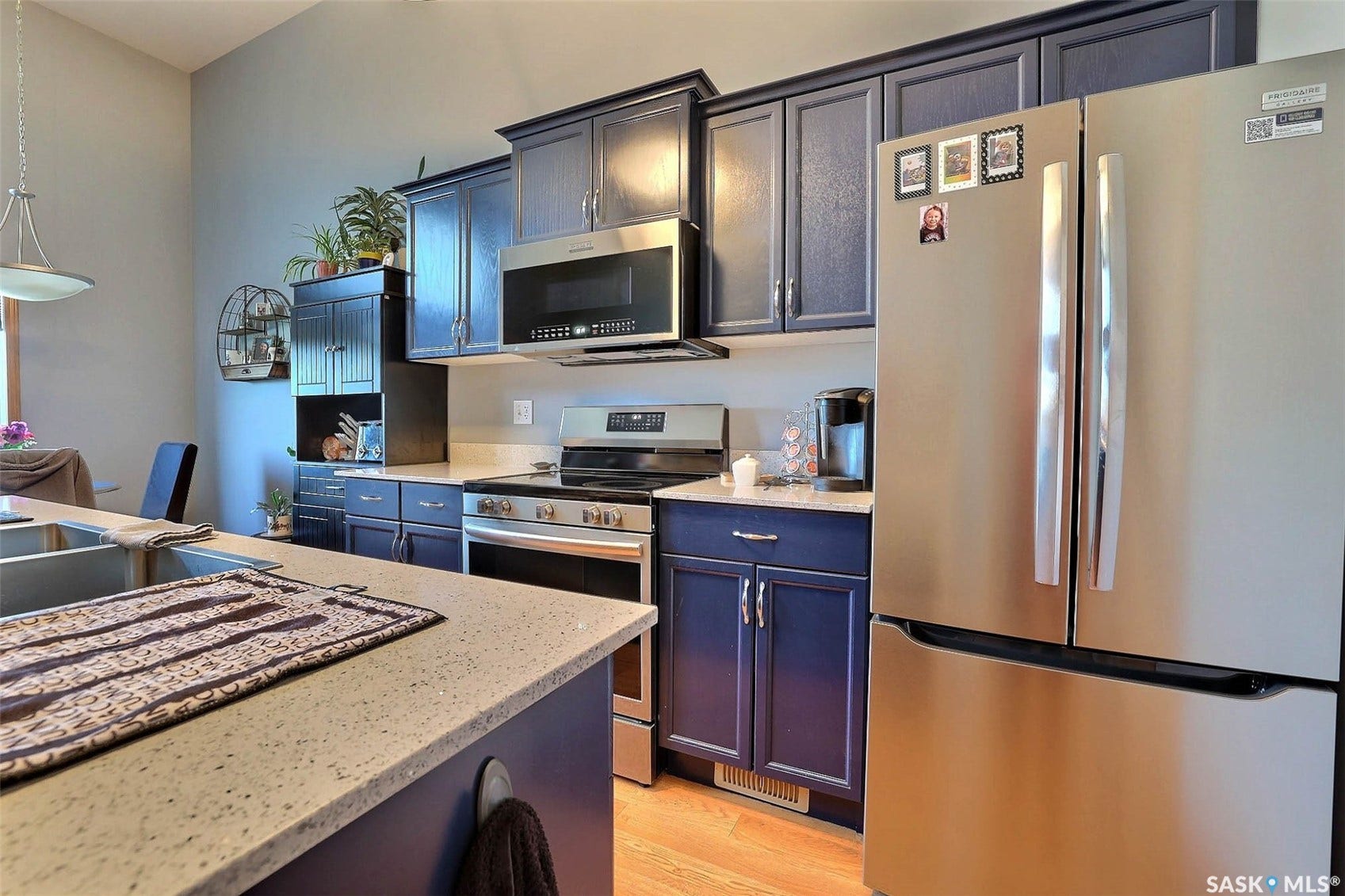 Kitchen featuring blue cabinetry, stainless steel appliances, granite countertops, wood-finish flooring, and a stainless steel sink