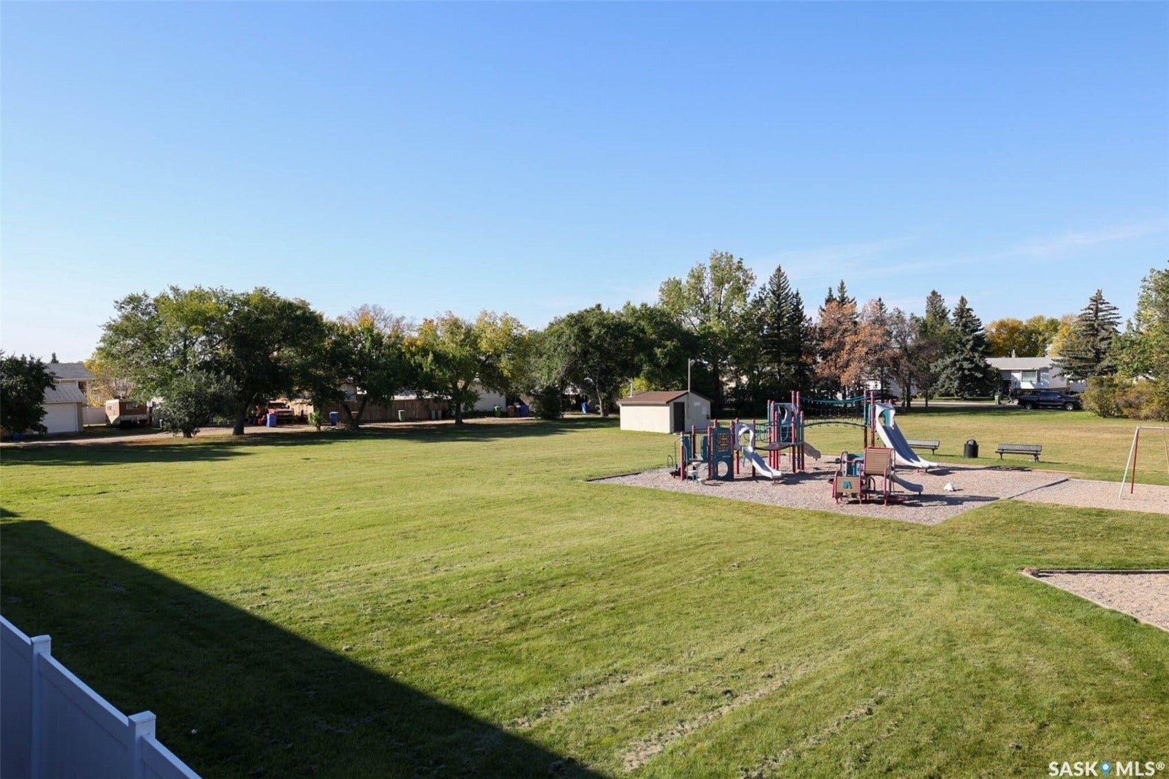 Expansive green space featuring a playground with slides and climbing structures, a sand area, and perimeter trees