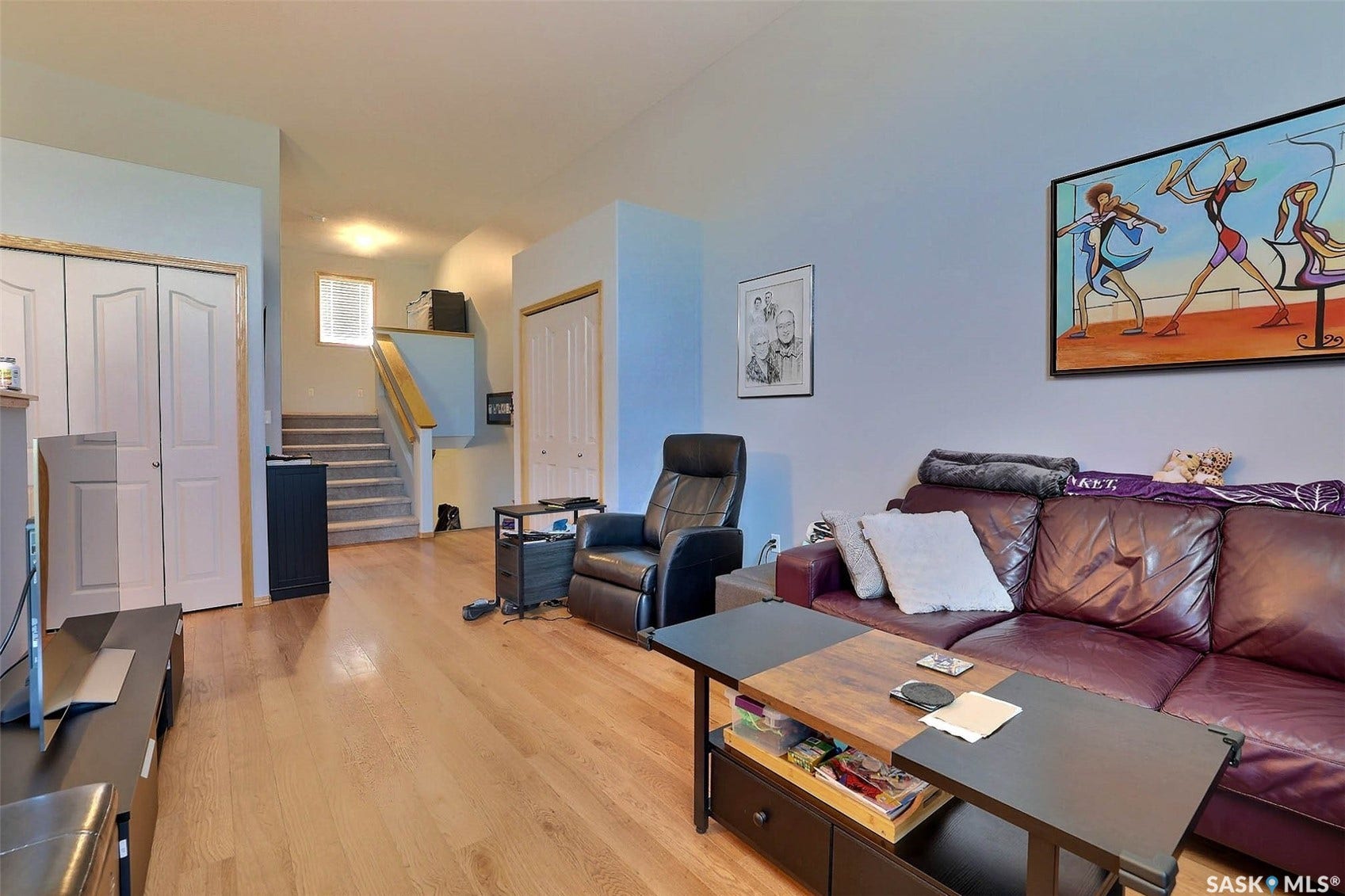 Open-concept living area featuring wood-finish flooring throughout, a burgundy leather sofa, and abundant natural light from multiple windows