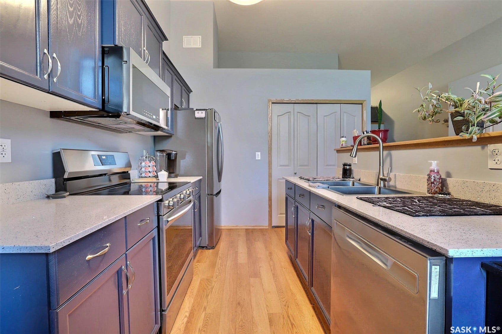 Kitchen featuring stainless steel appliances, dark cabinetry, light-toned countertops, and wood-finish flooring
