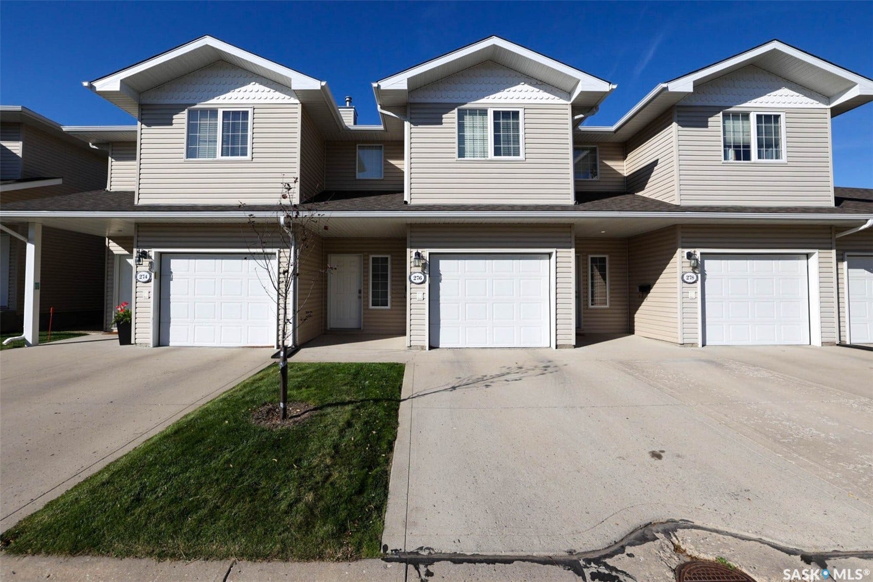 Multi-unit residential structure featuring light-colored horizontal siding, multiple gabled dormers, attached garages with white panel doors, and concrete driveways