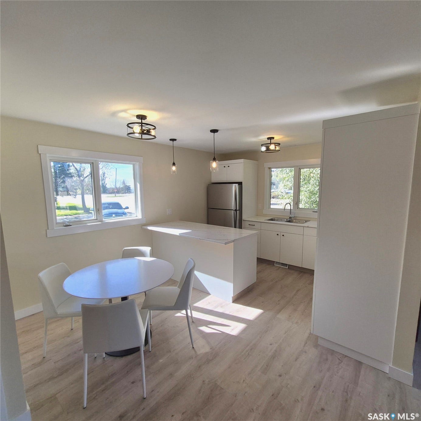 Open-concept kitchen and dining area featuring light wood-finish flooring, white cabinetry, a central island with a white countertop, and stainless steel appliances