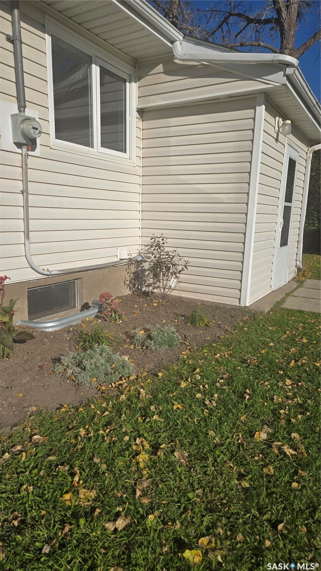 Cream-colored vinyl siding exterior with white trim accents and a window well