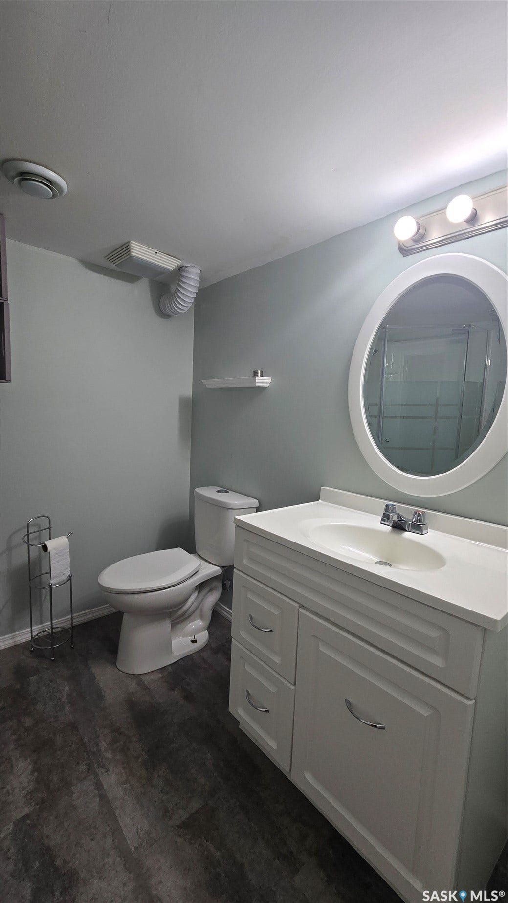 Bathroom featuring a white vanity with integrated sink, oval mirror, wall-mounted lighting, and wood-finish flooring
