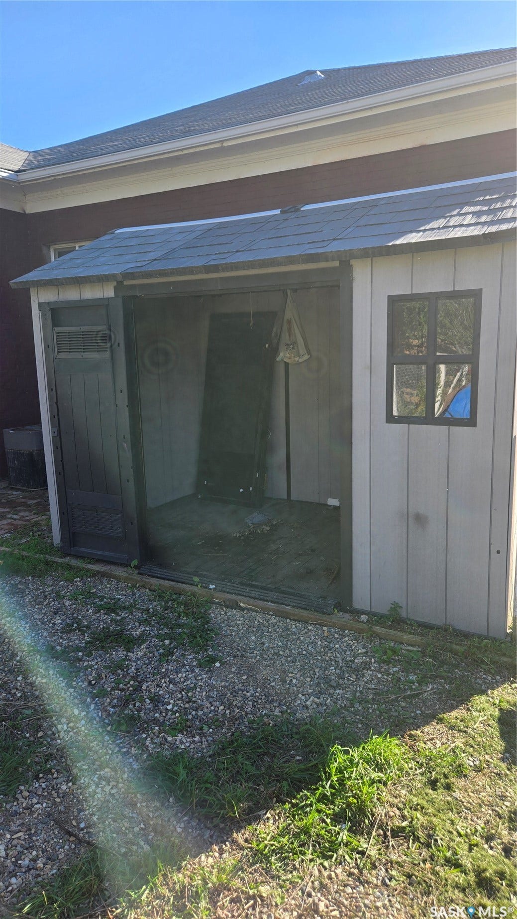 Detached storage shed with a shingled roof, light-colored siding, and a single window