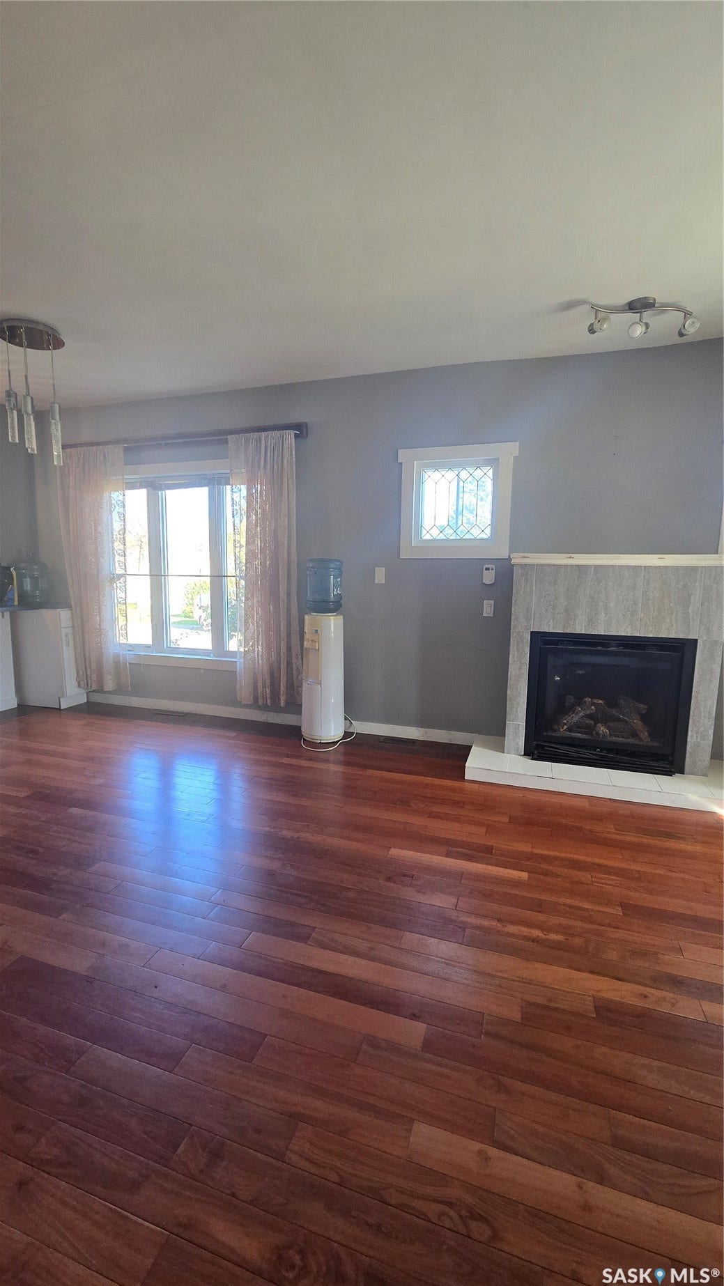 Hardwood flooring throughout, a gas fireplace with a tiled surround, a large window, and a decorative upper window