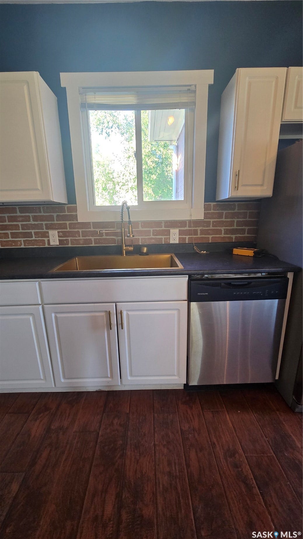 White cabinetry, a bronze-finish sink, dark countertops, a brick-patterned backsplash, and wood-finish flooring