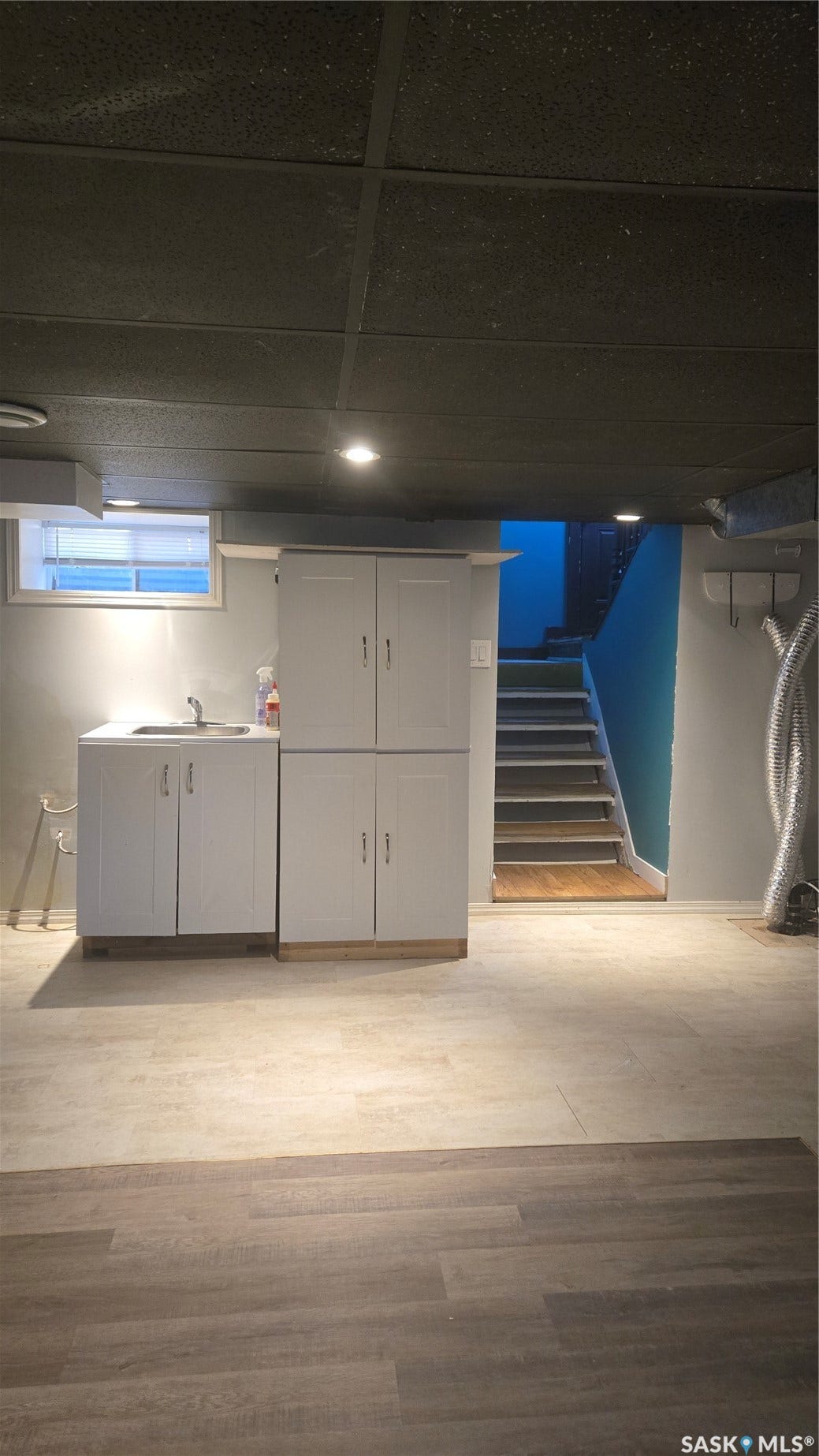 White cabinetry with integrated sink, recessed lighting, varied wood-finish flooring, and painted staircase