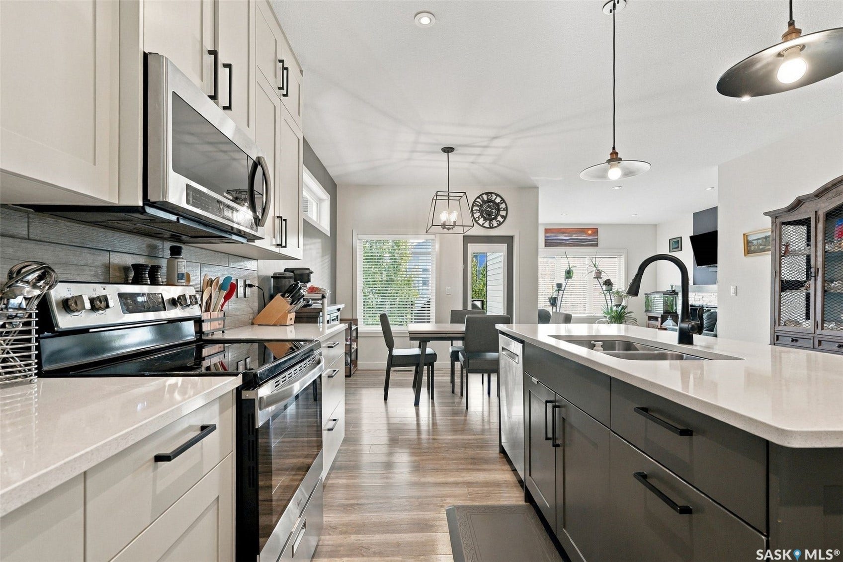 Kitchen featuring stainless steel appliances, light-toned upper cabinetry, dark lower cabinetry, an island with a sink, and wood-finish flooring