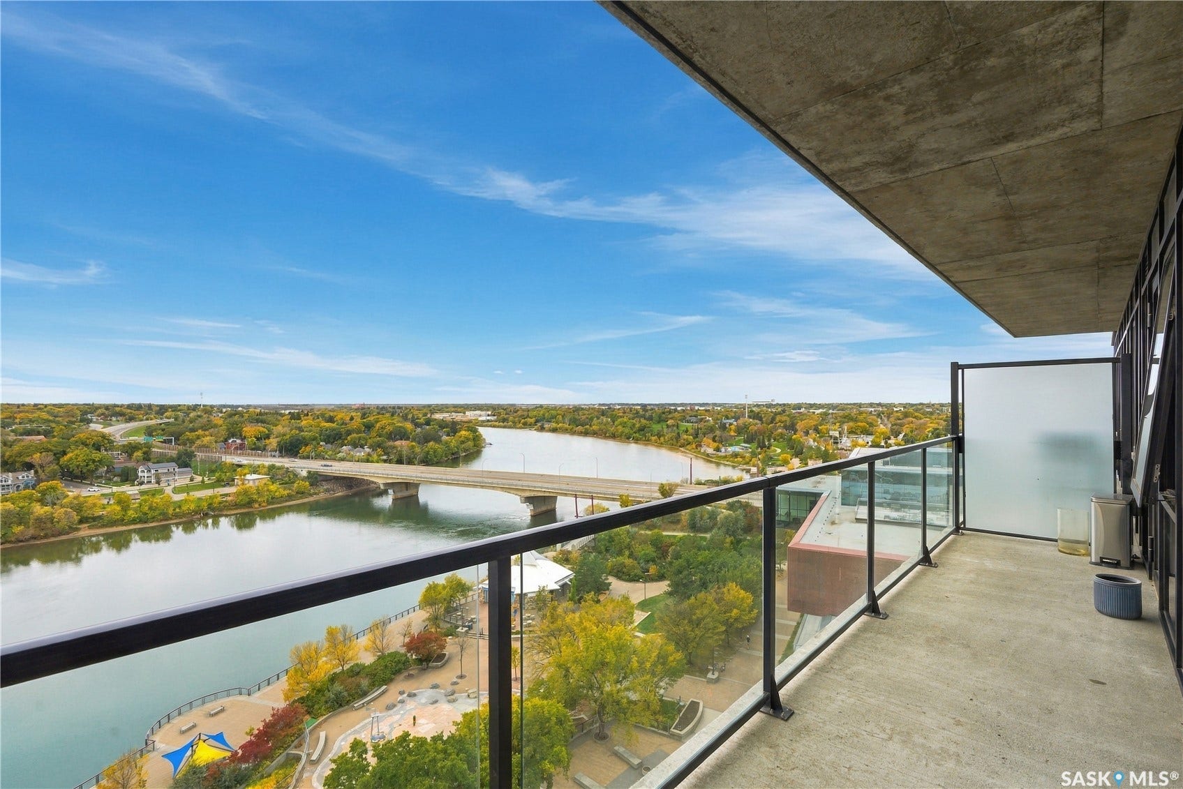 Concrete balcony with black metal and glass railing, featuring expansive water and bridge scenery