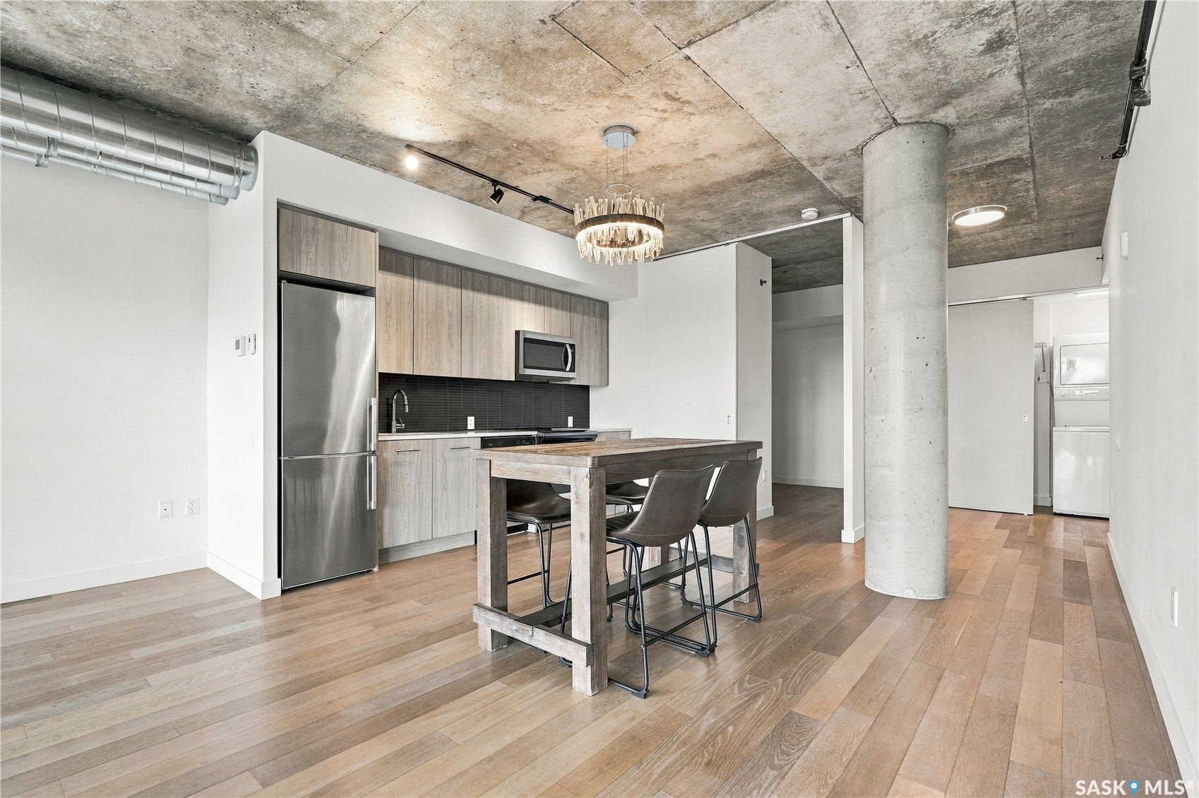 Open-concept living area with concrete ceiling and pillar, wood-finish flooring, and a modern kitchen featuring stainless steel appliances