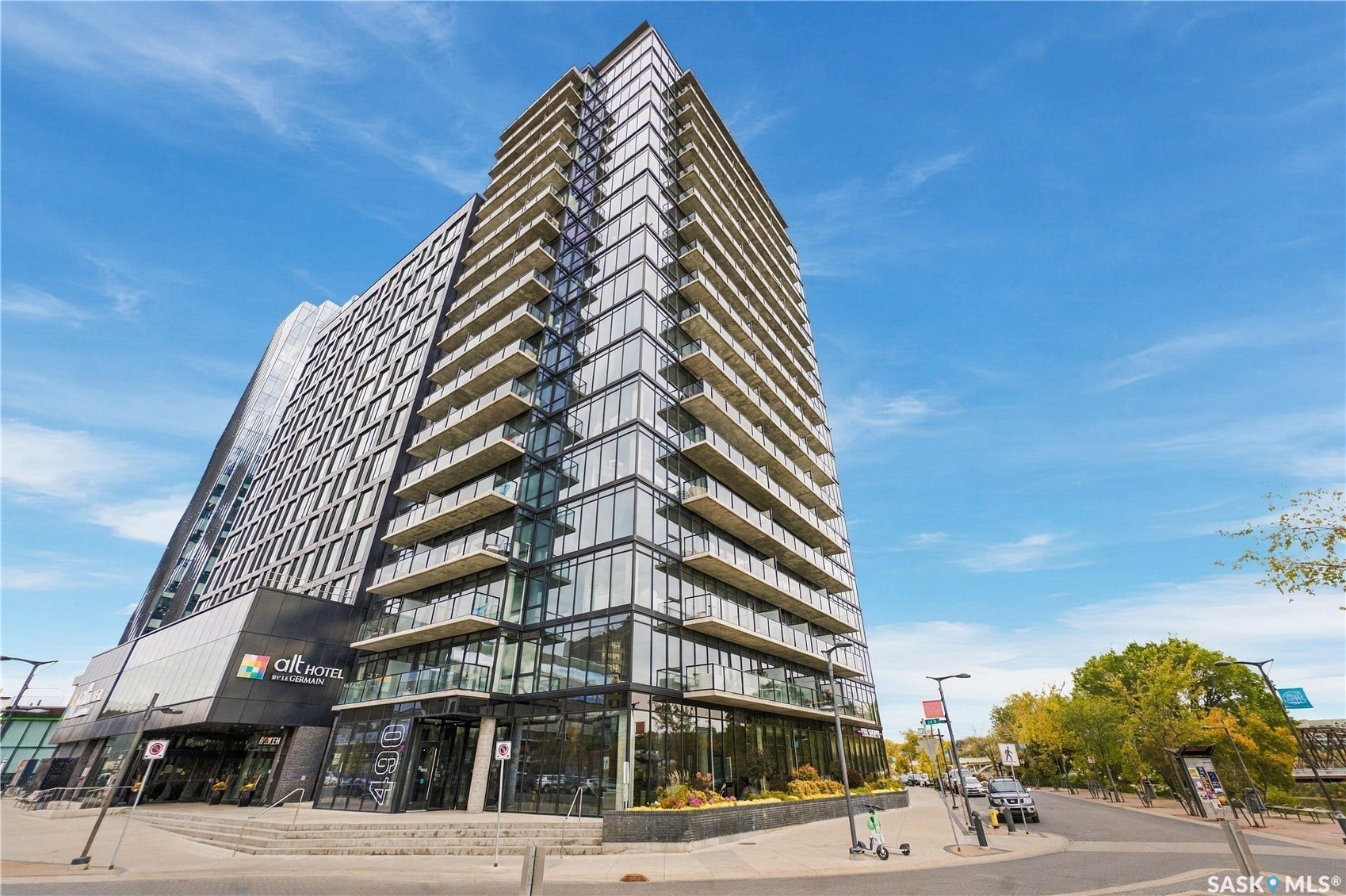 Modern high-rise building with a glass facade, multiple private balconies, and ground-level commercial spaces