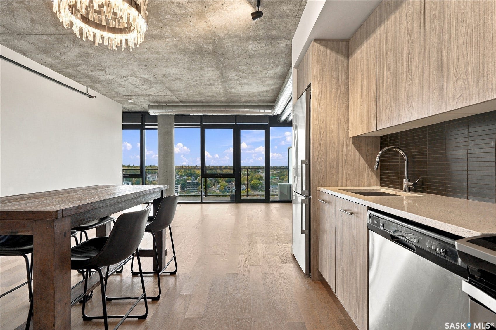 Modern kitchen featuring light wood-finish cabinetry, stainless steel appliances, and a dark tile backsplash