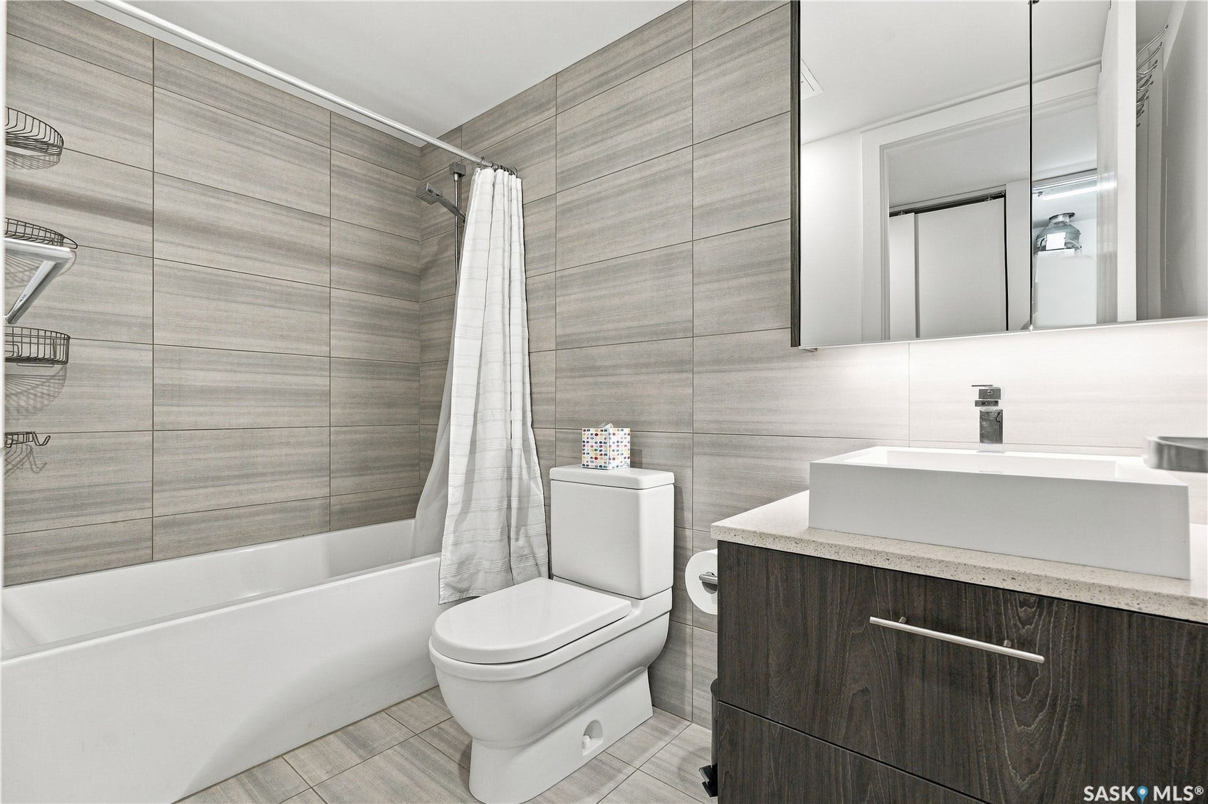 Full bathtub with a tiled surround, wood-finish vanity with a vessel sink, and a mirrored medicine cabinet