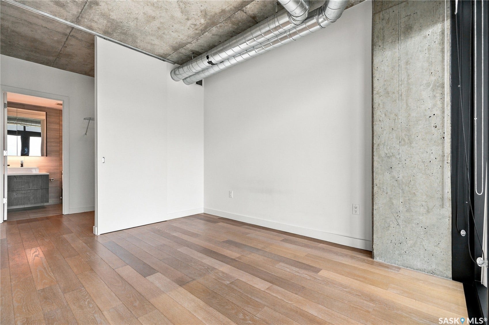 Exposed concrete ceiling with visible ductwork, wood-finish flooring, and a large sliding panel door
