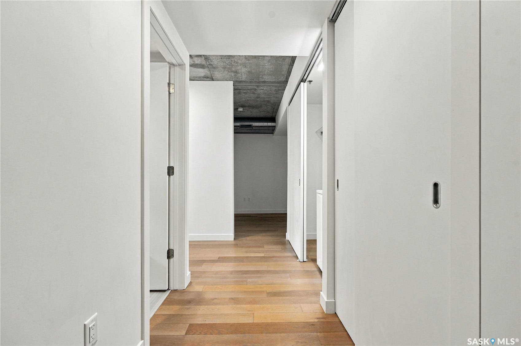 Wood-finish flooring throughout, exposed concrete ceiling, white interior doors, and a modern sliding door system