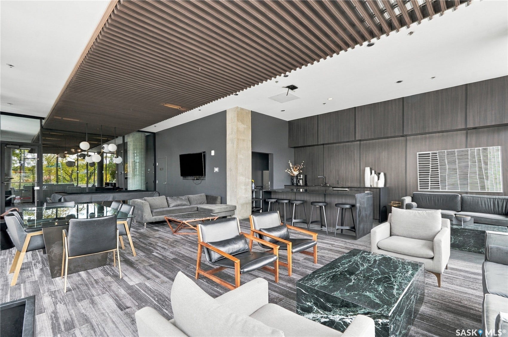 Open-concept communal area featuring a wood-slat ceiling accent, full-height wall paneling, a built-in bar with seating, and large-format flooring