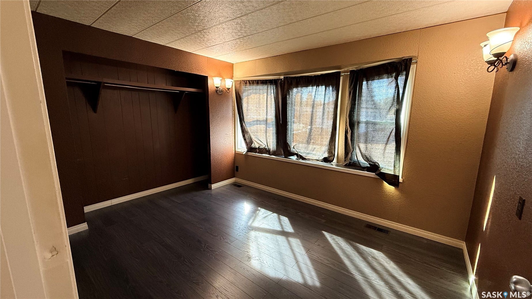 Wood-finish flooring, built-in closet with shelving, multiple windows, and dual wall-mounted light fixtures
