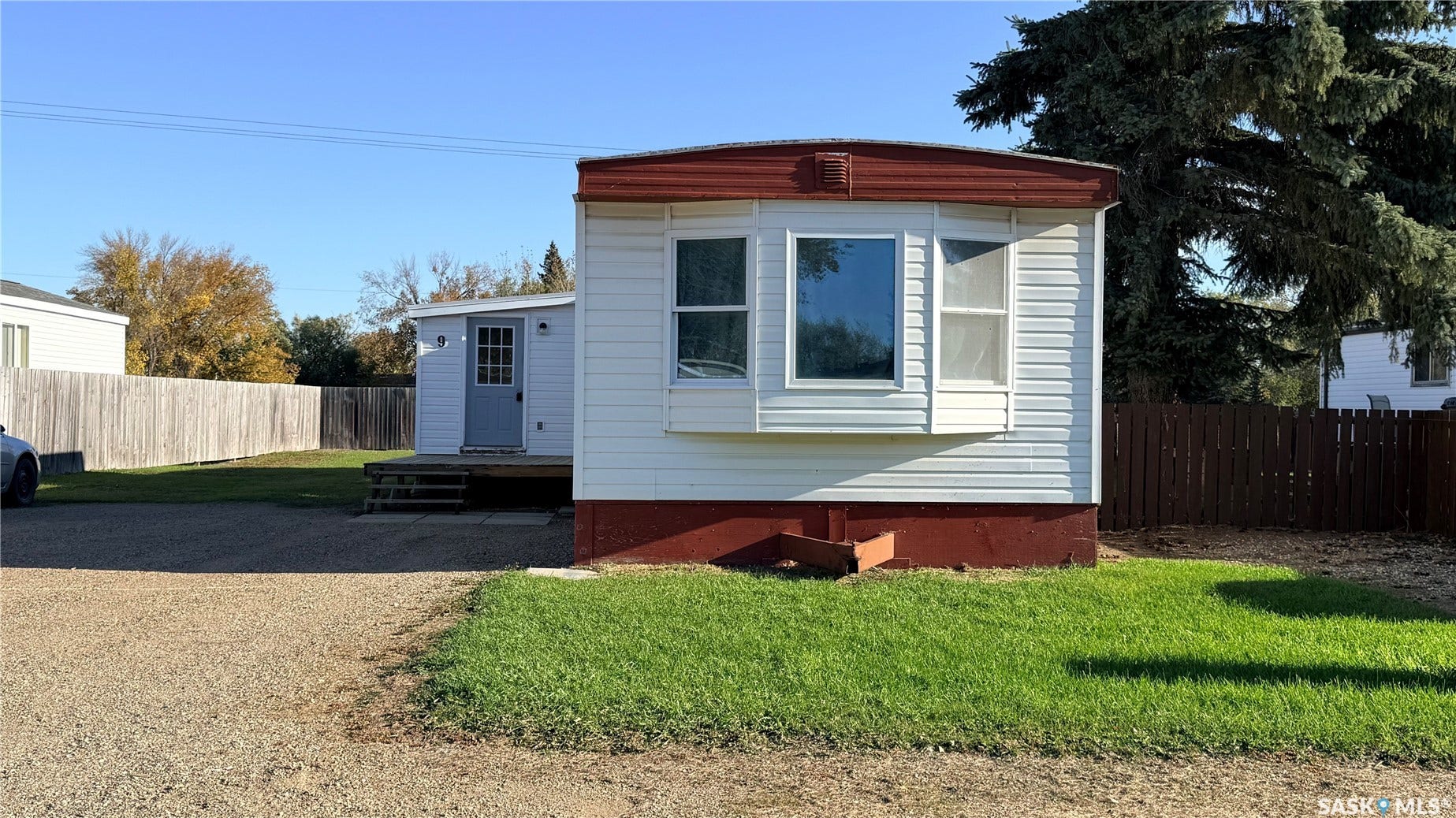 White siding exterior with a red trim roof, bay window, gravel driveway, and a fenced yard