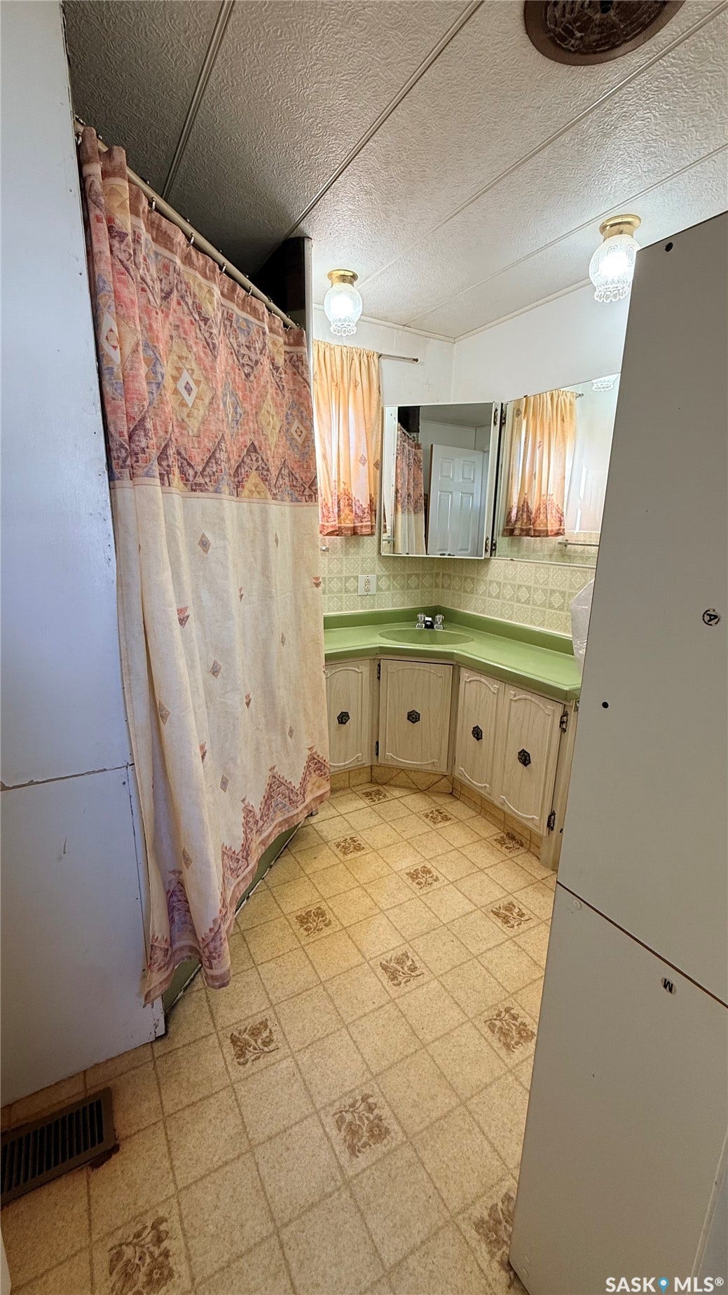 Patterned tile flooring, corner vanity with a green countertop, dual wall-mounted light fixtures, and a mirrored medicine cabinet