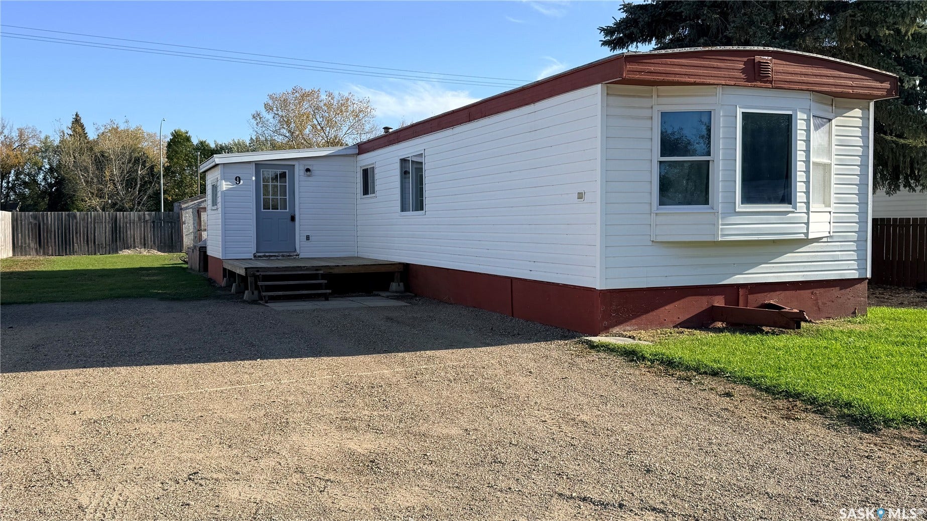 White siding exterior with a red trim roof, bay window, and a gravel driveway