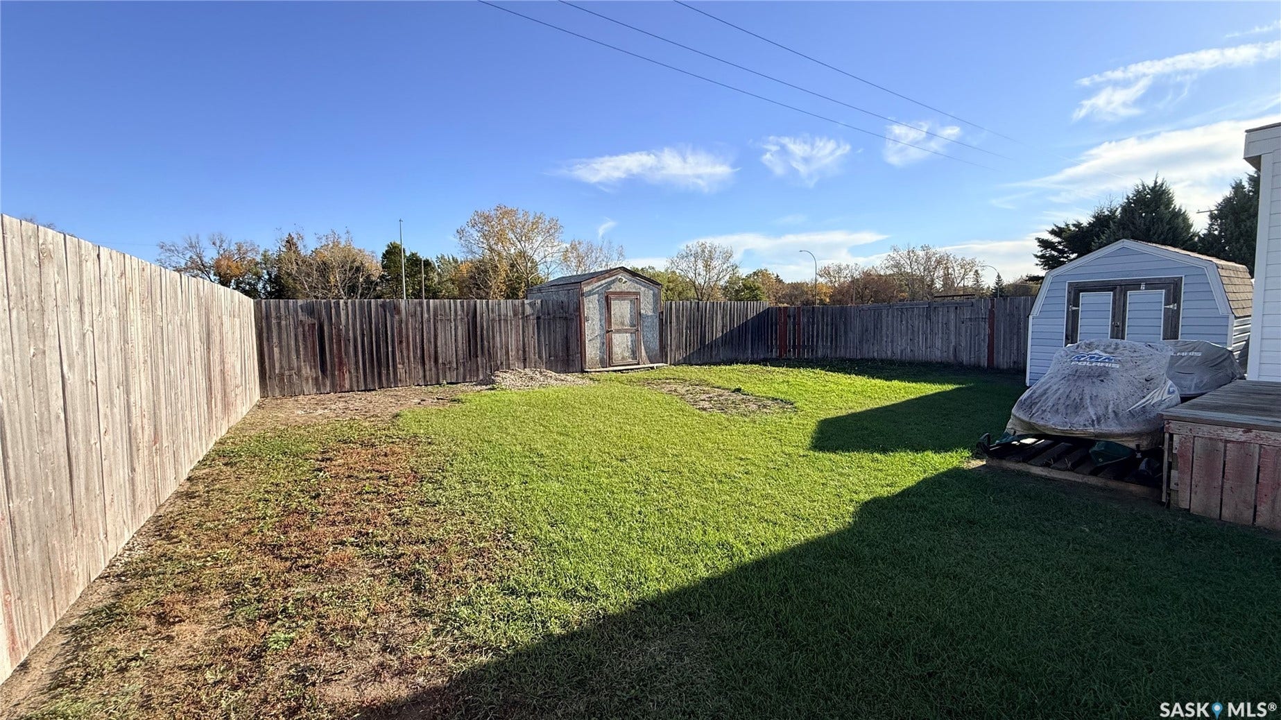Expansive backyard featuring a manicured lawn, full wood fencing, a light blue storage shed, and an additional wood storage shed