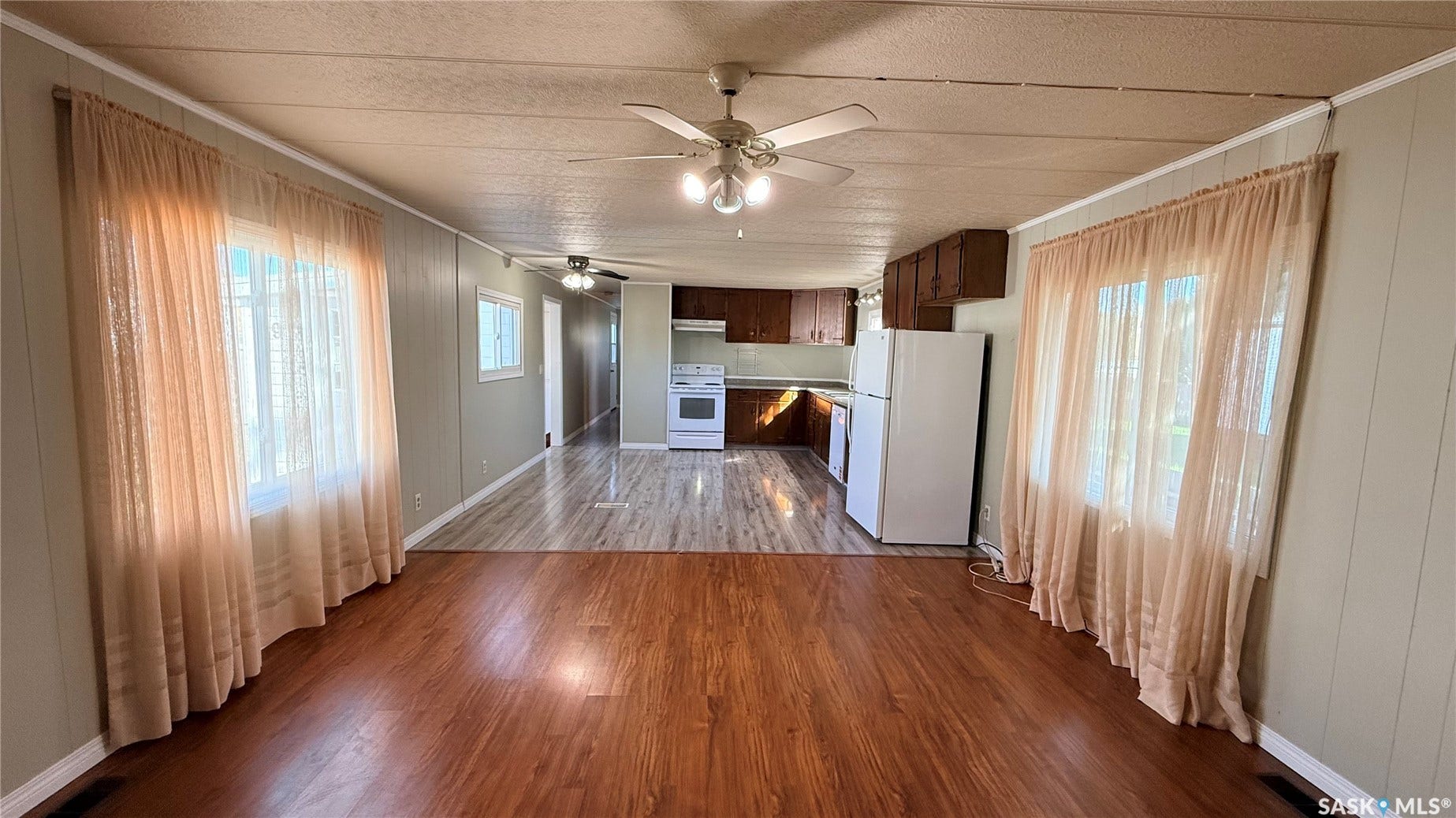 Wood-finish flooring throughout, ceiling fans with integrated lighting, and white appliances with dark wood cabinetry