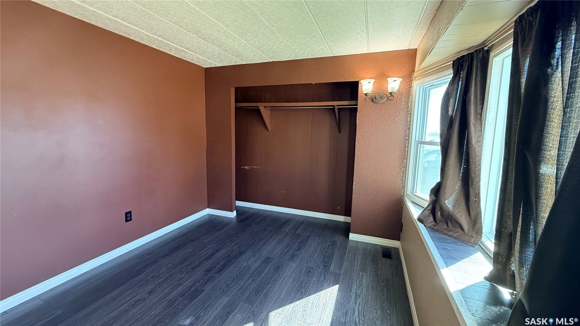 Wood-finish flooring, built-in closet with shelving, multiple windows, and wall-mounted sconce